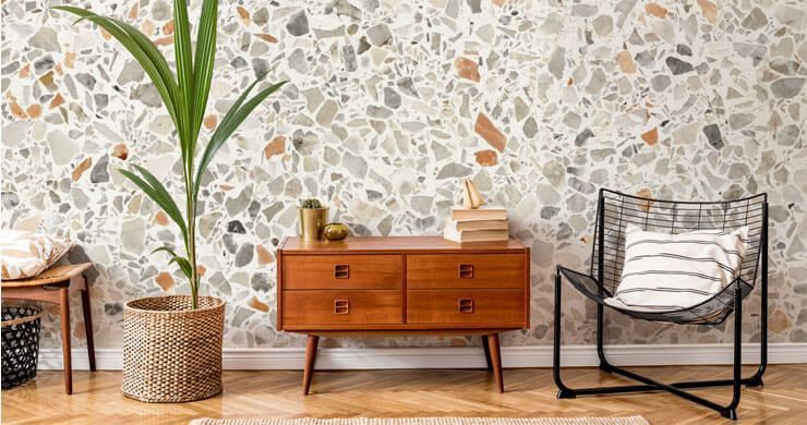 Interior with a mid-century wooden dresser, houseplant, patterned wallpaper, and chair with pillow.