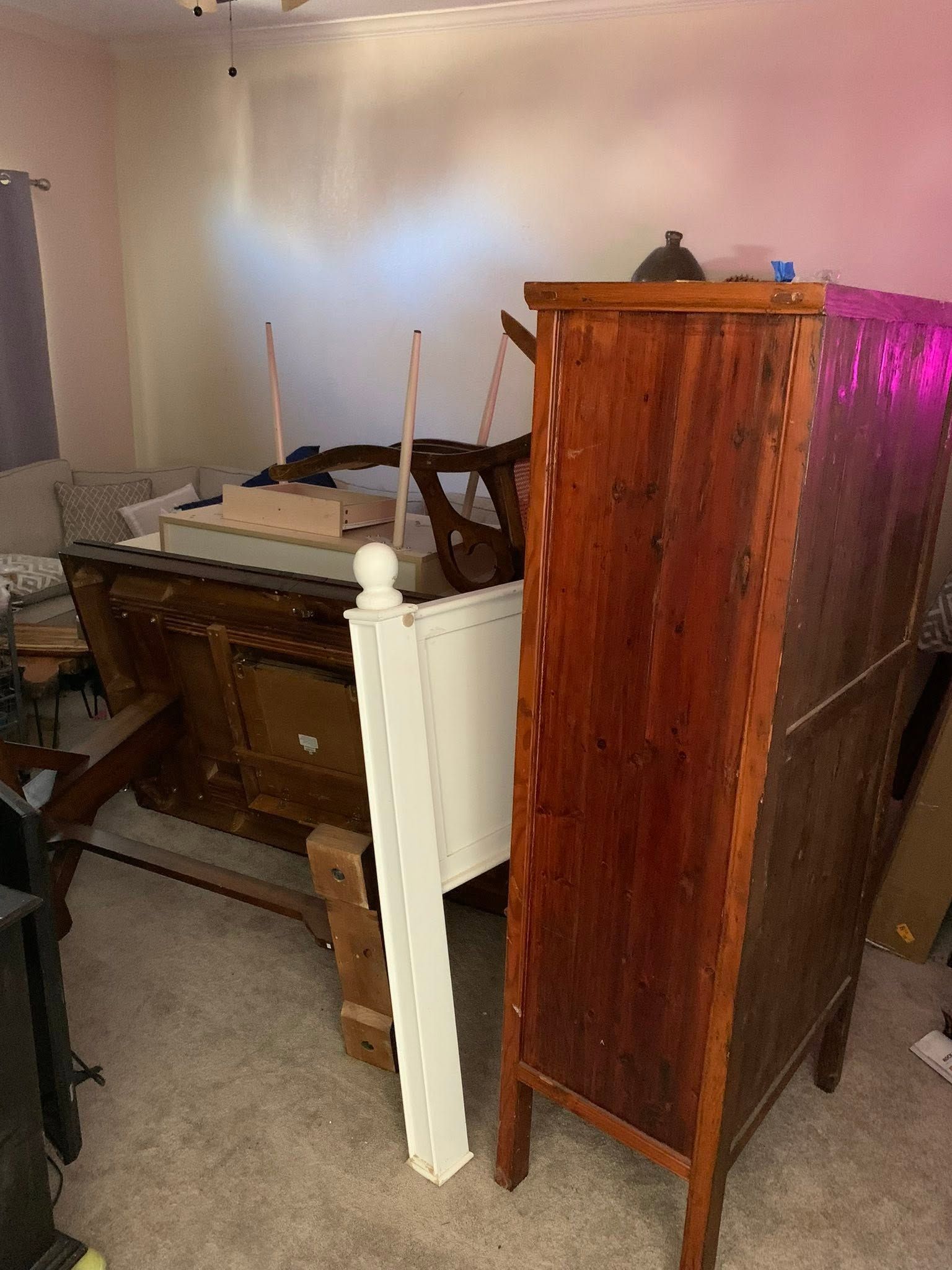 Cluttered room with a wooden cabinet, dresser, and white bedframe leaning against a wall.