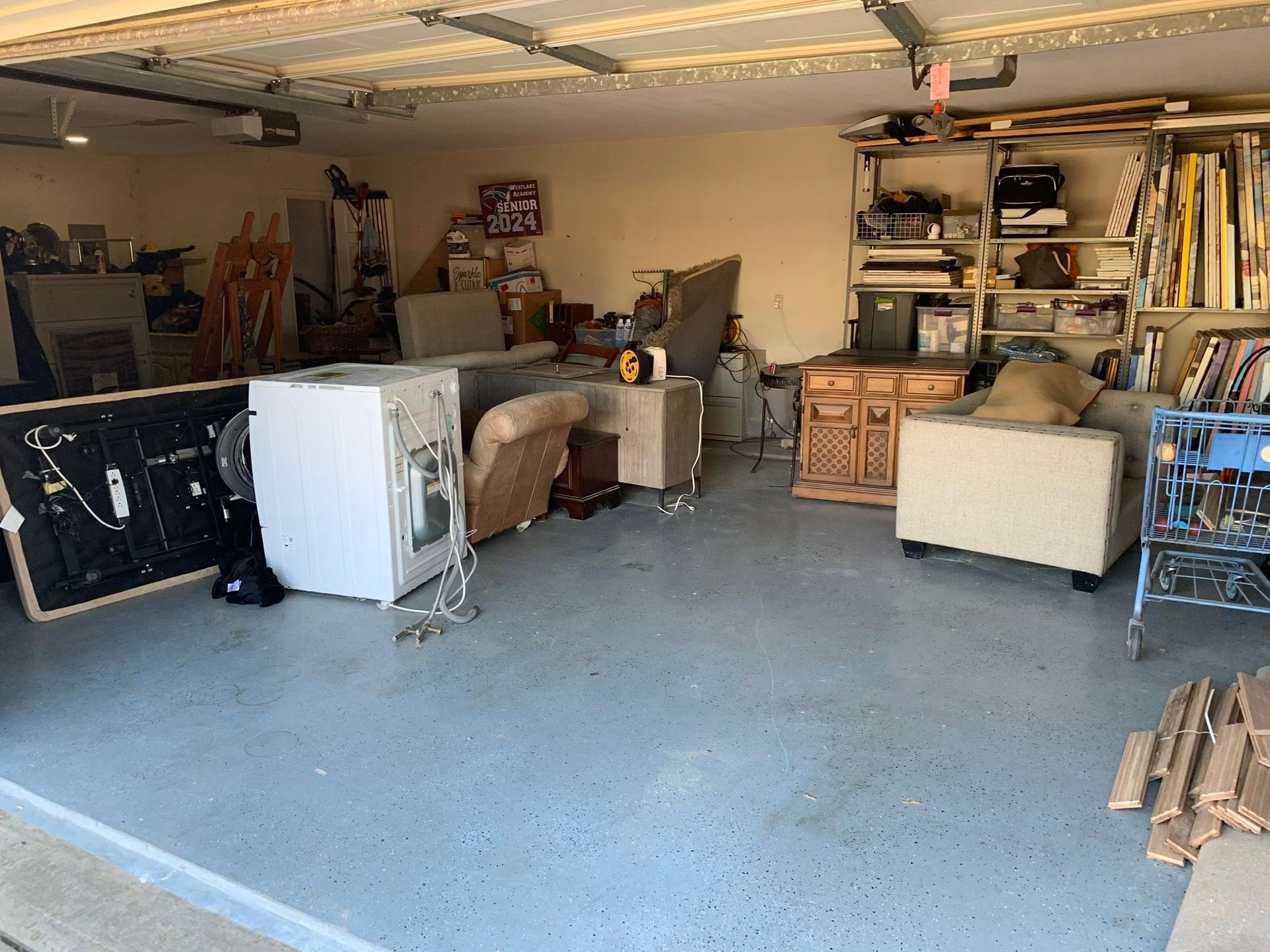 Cluttered garage with couches, shelves, and a white appliance on a concrete floor