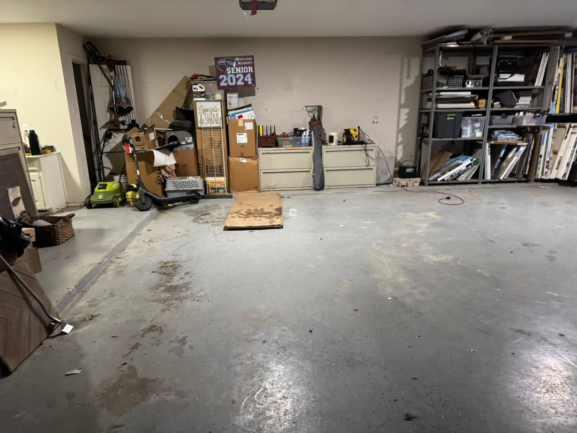 Cluttered garage with shelves, boxes, tools, and a concrete floor