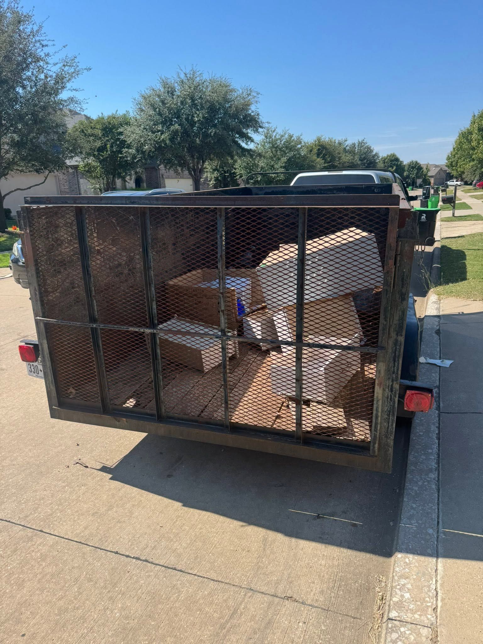 Open utility trailer with folded metal furniture and boxes parked on a sunny street