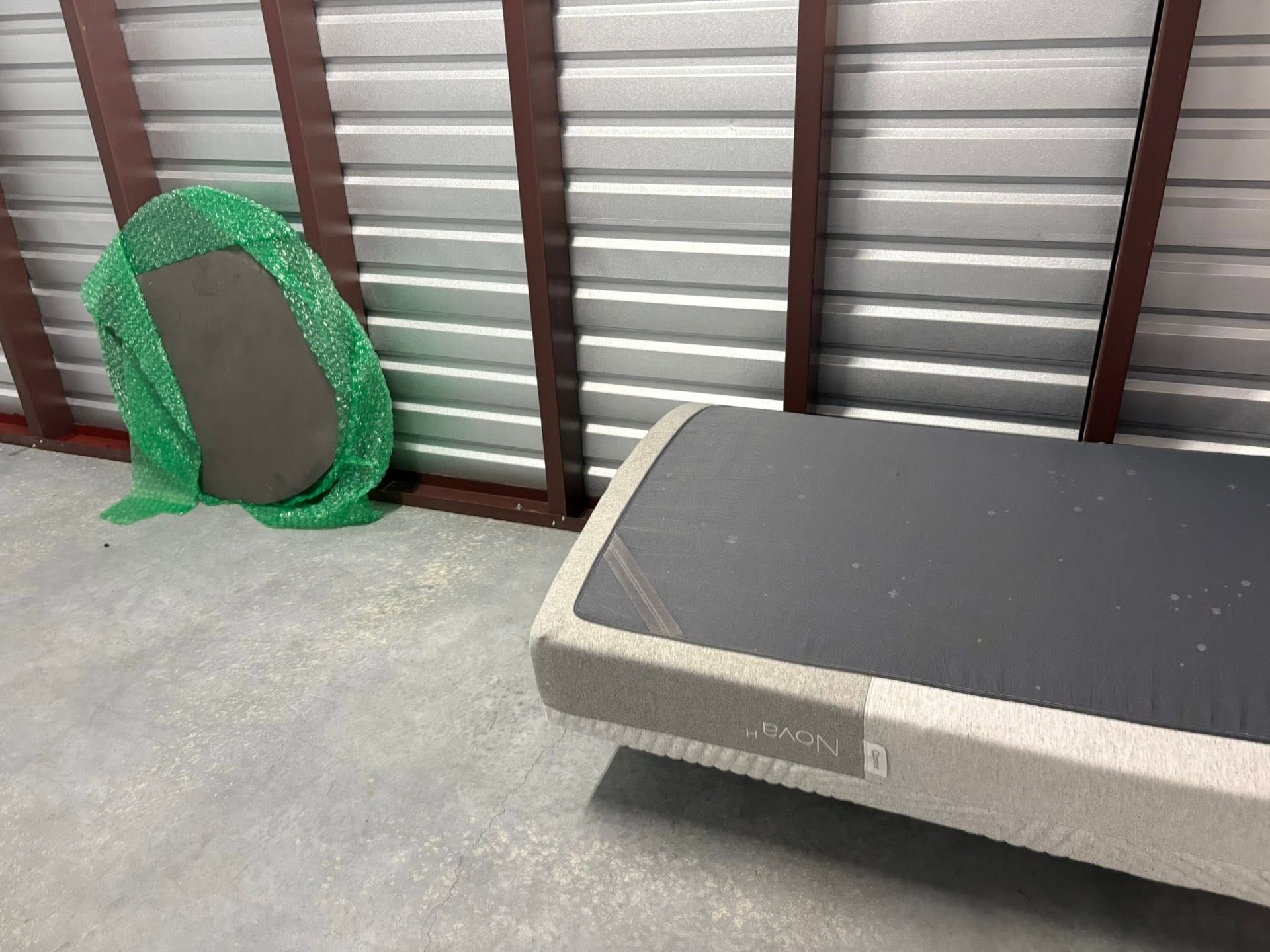 Mattress on the floor beside a green pet bed against a corrugated metal wall.