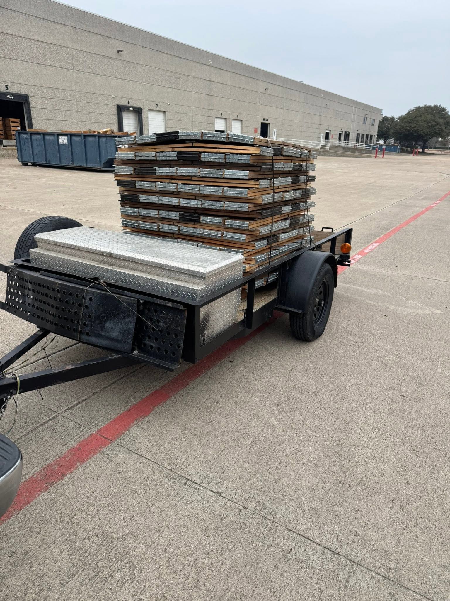 Trailer stacked with broken pallets and debris in a parking lot beside a warehouse