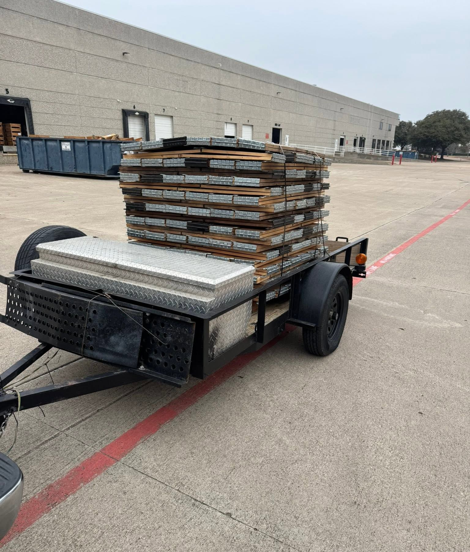 Trailer loaded with stacked pallets in a parking lot beside a warehouse