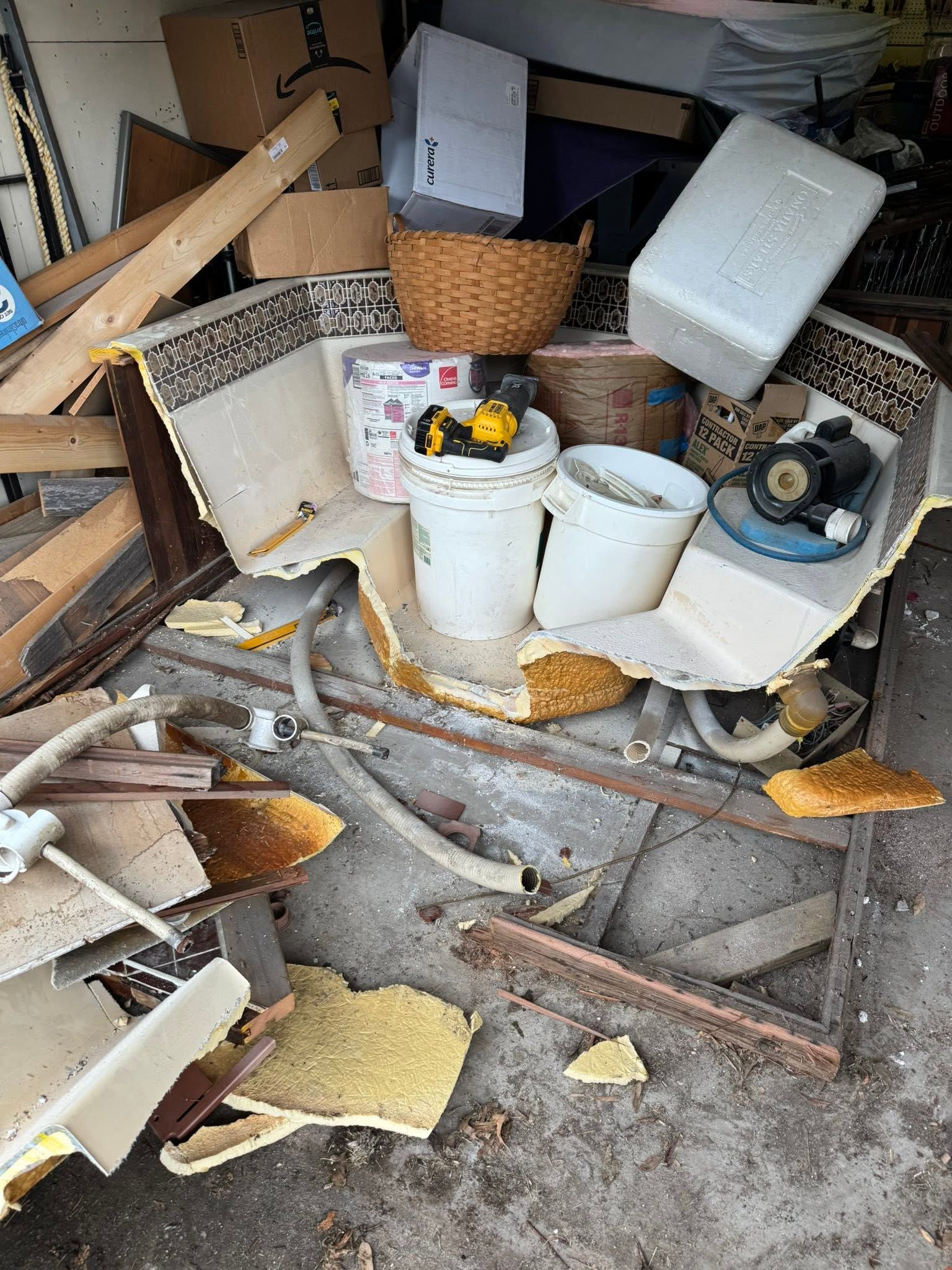 Cluttered storage area with broken furniture, scattered debris, and overturned buckets on a concrete floor