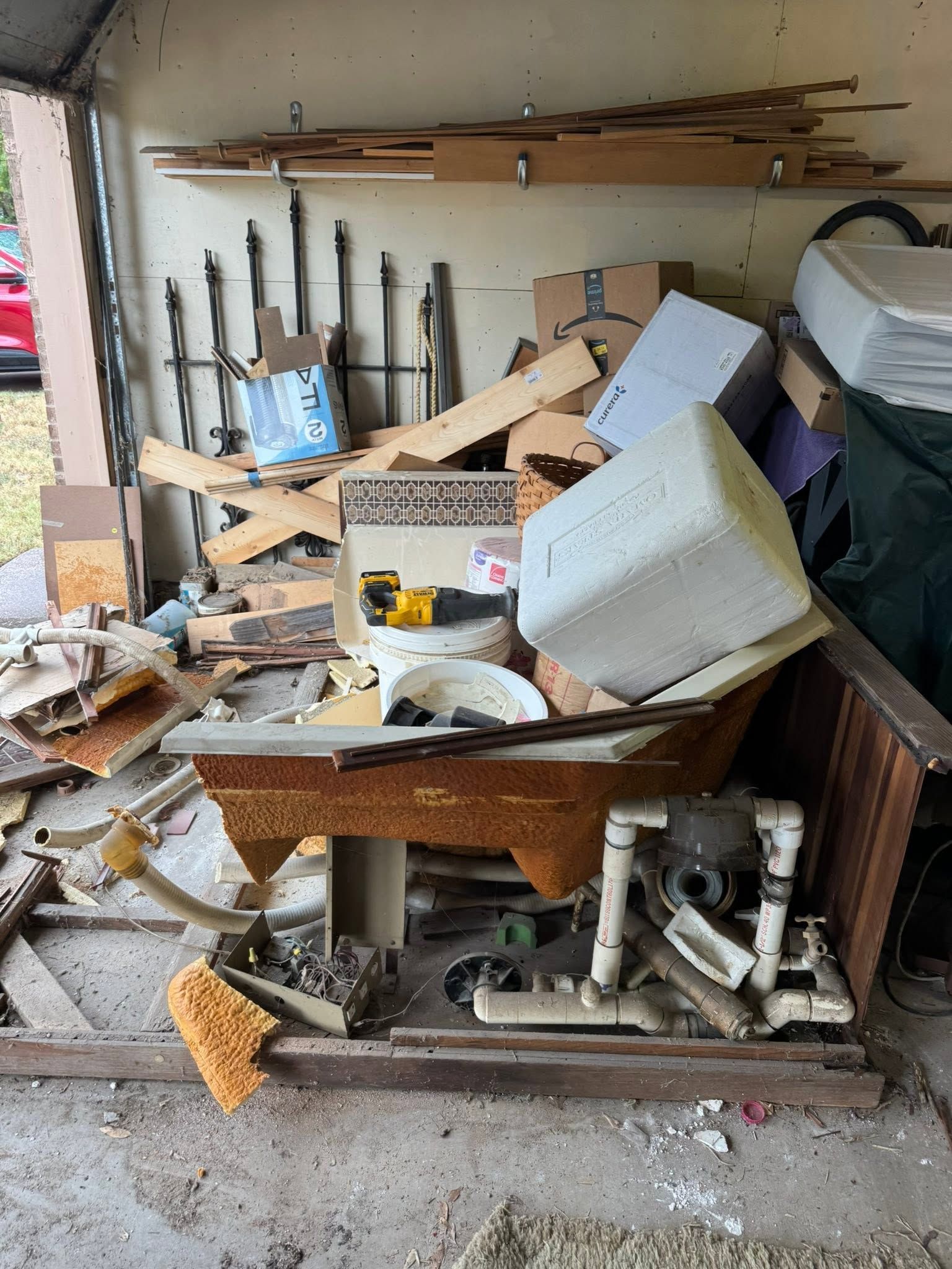 Cluttered garage with broken furniture, scattered debris, and tools stacked against the wall