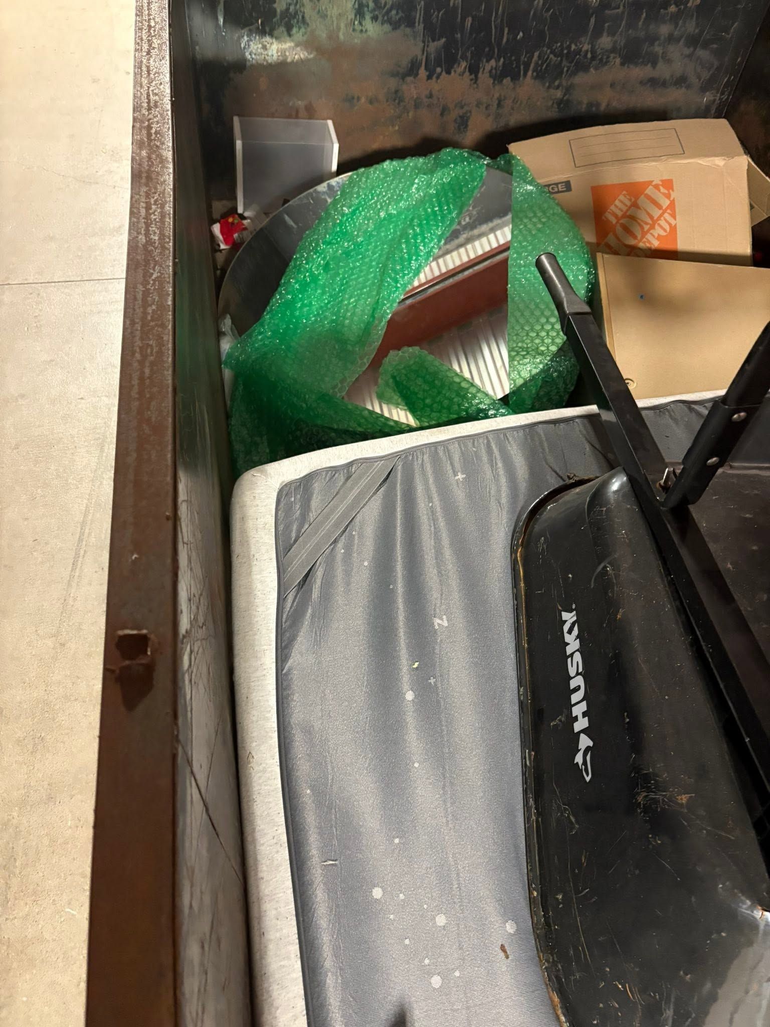 Gray duffel bag, green mesh bag, and cardboard box stuffed in a narrow storage space