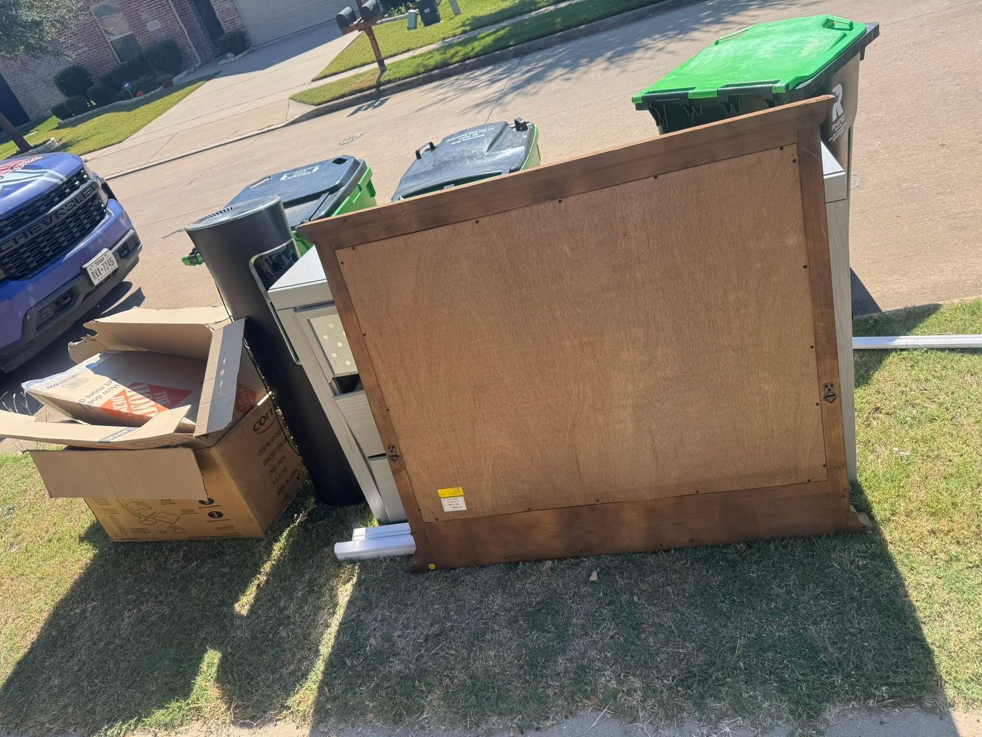 Discarded furniture and trash bins beside a curb in a residential area