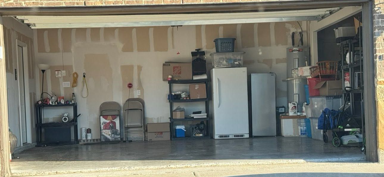 Open garage with shelves, white refrigerator, storage bins, and tools along the back wall.