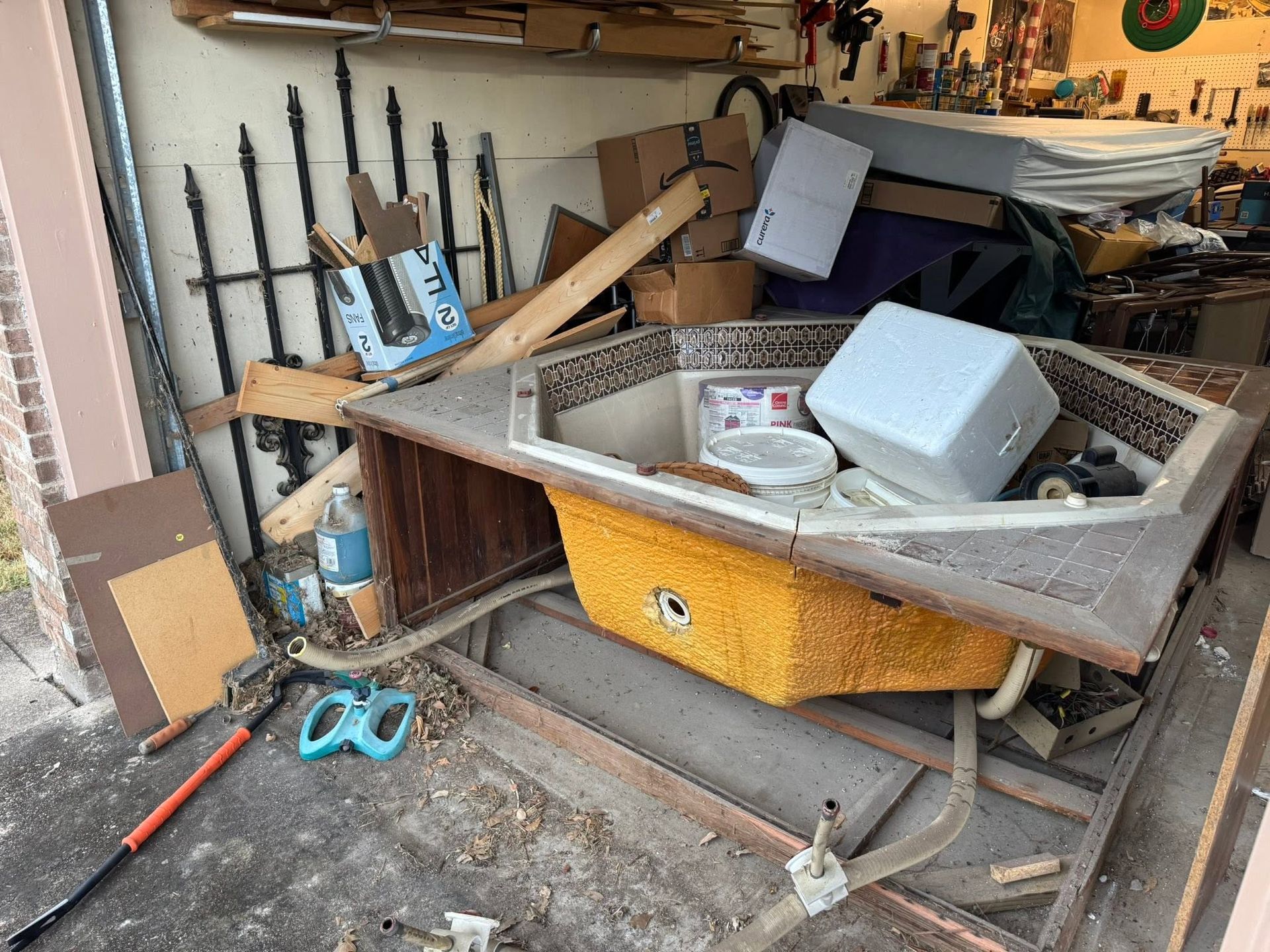 Cluttered garage with a wheelbarrow, tools, pipes, and scattered debris on the floor.