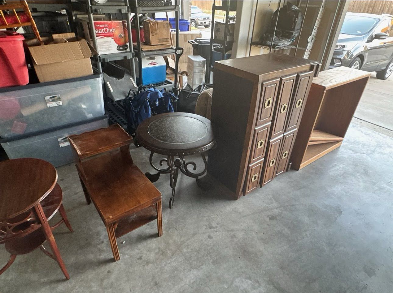 Assorted vintage furniture, including chairs, a round table, and cabinets, displayed in a shop or warehouse.