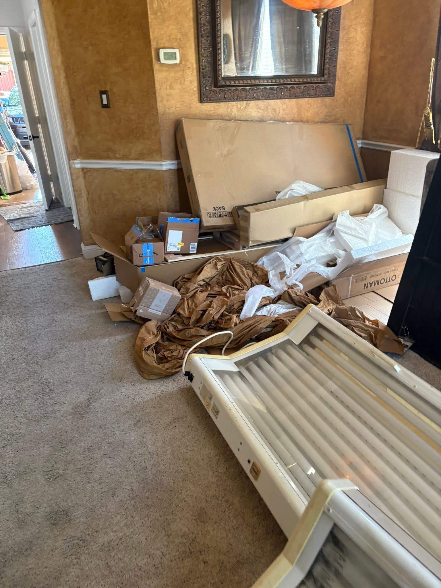 Damaged room with debris, a fallen white door, and scattered packing materials on carpet.