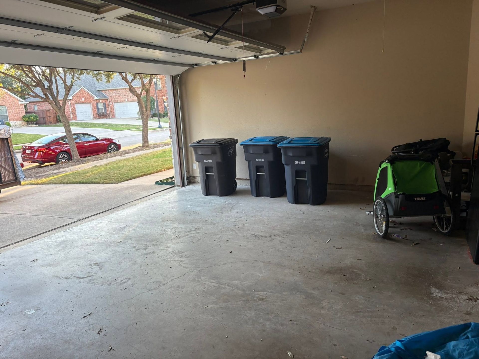 Open garage with trash bins by the wall and a green stroller or cart near the right side.