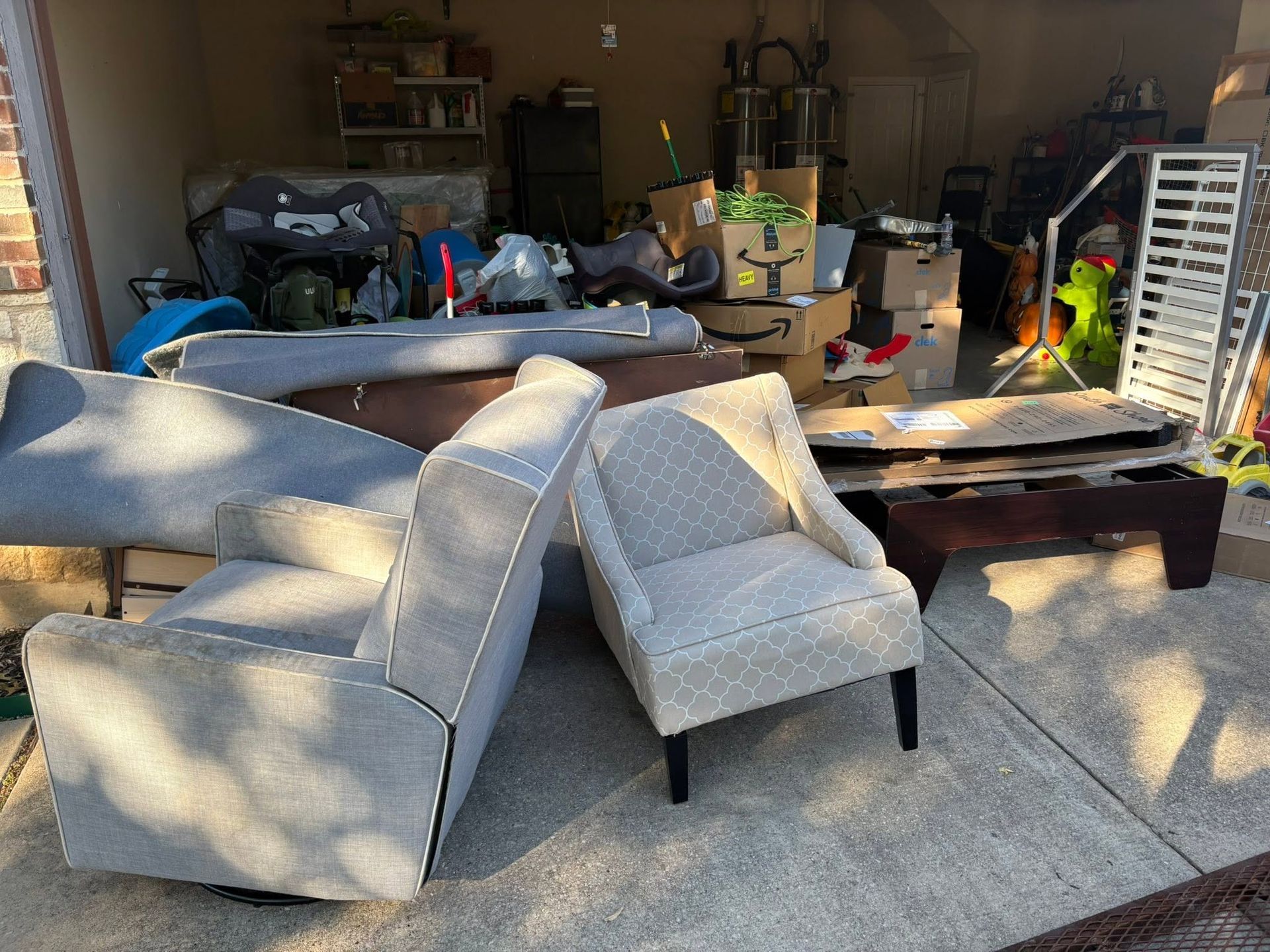 Couch and armchair on a patio beside a cluttered garage with boxes, tools, and outdoor items.