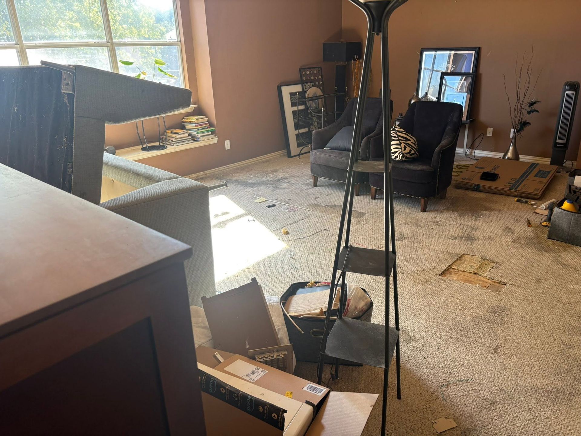 Cluttered living room with overturned chair, scattered debris, mirror, and bright sunlight from a window