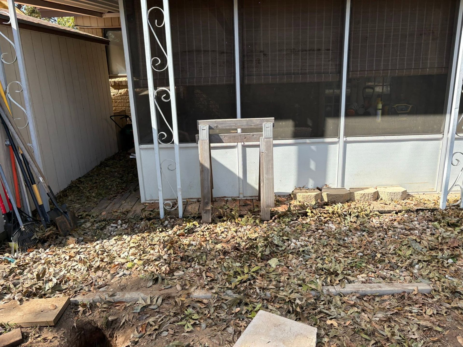 Backyard with leaf-covered ground, shed siding, and a small wooden stand near a screened porch.