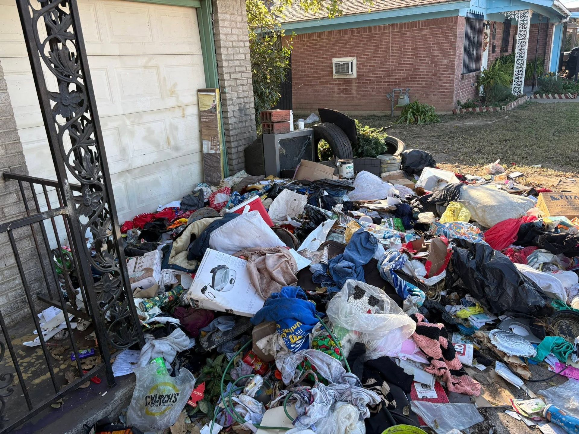 Overflowing trash bags and scattered rubbish piled beside a garage and fence in a yard