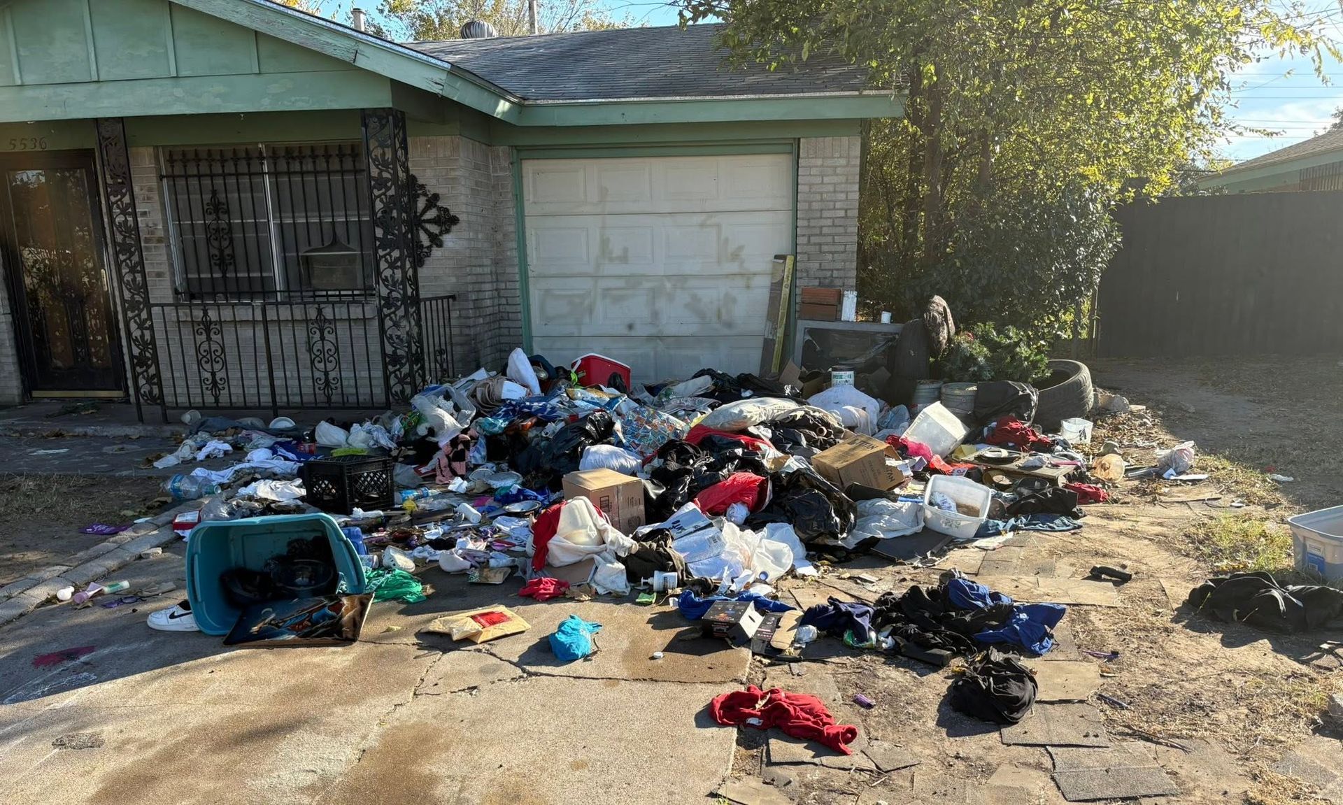 Pile of trash scattered across a front yard near a house and garage in daylight.