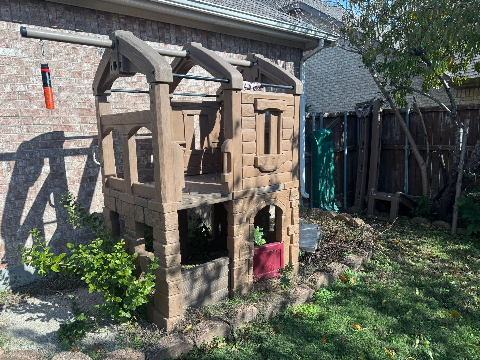 Wooden outdoor playhouse beside a brick house, with a small figure in the lower doorway.