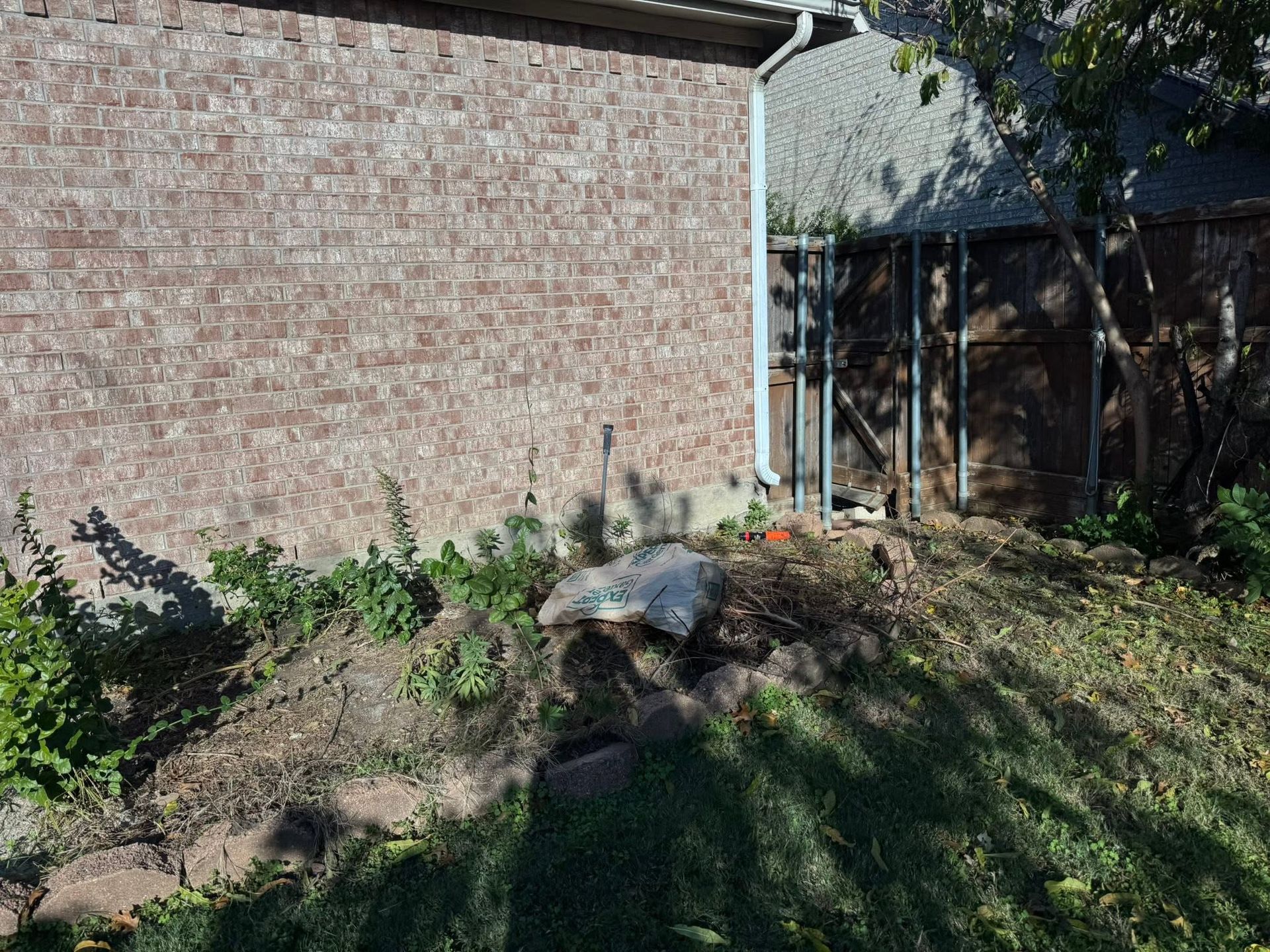 Backyard dirt mound beside a brick house, with patchy grass and trees in the background