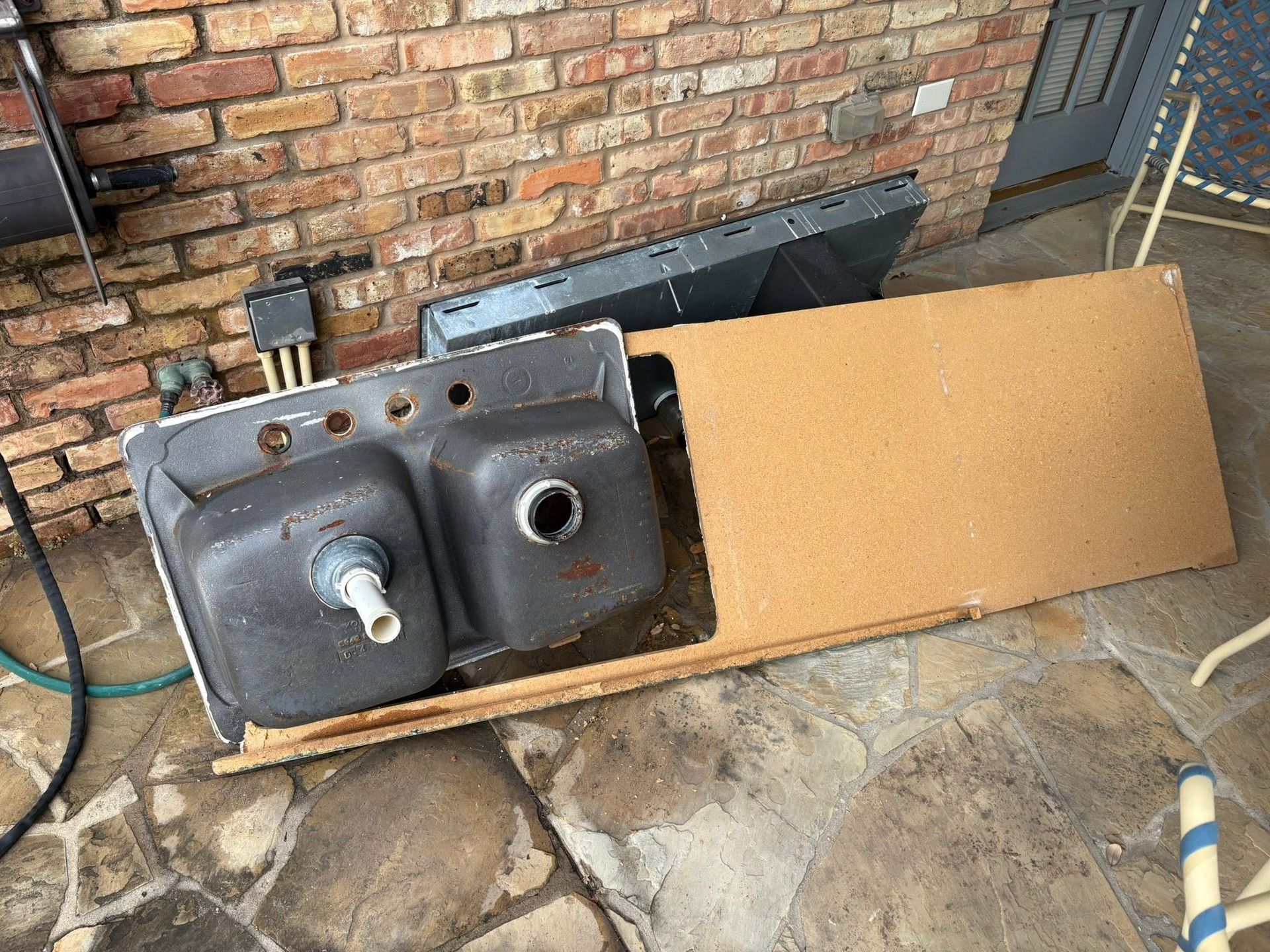 Black metal sink on cardboard beside brick wall, with exposed plumbing fixtures and a metal backsplash.