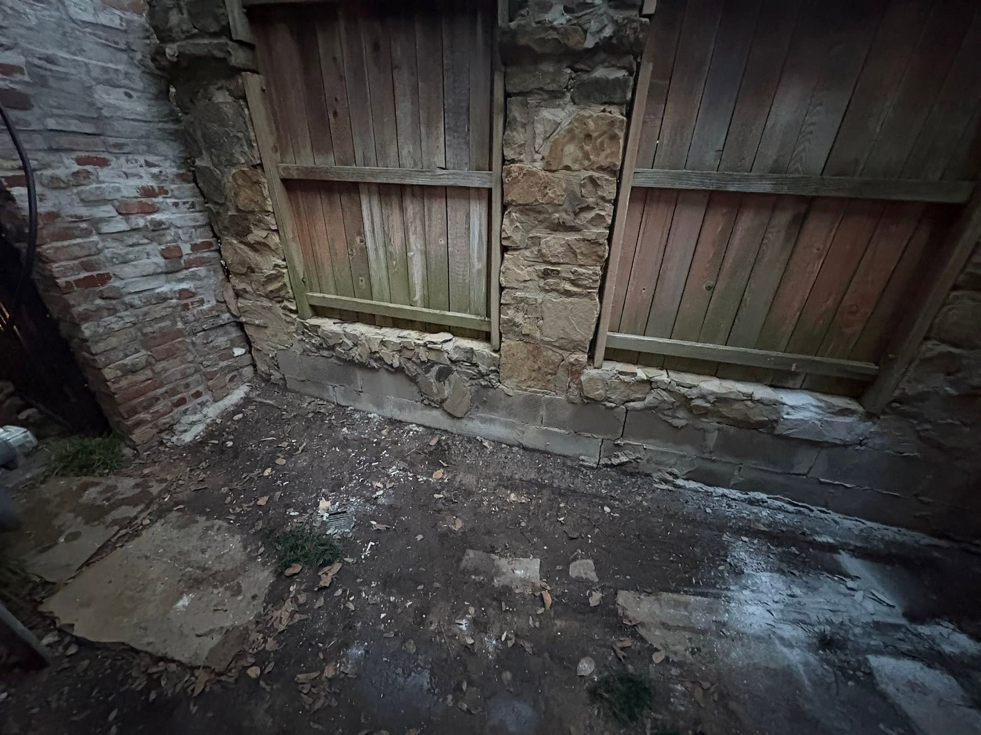 Damp, muddy alley beside a brick wall and weathered wooden fence gates.