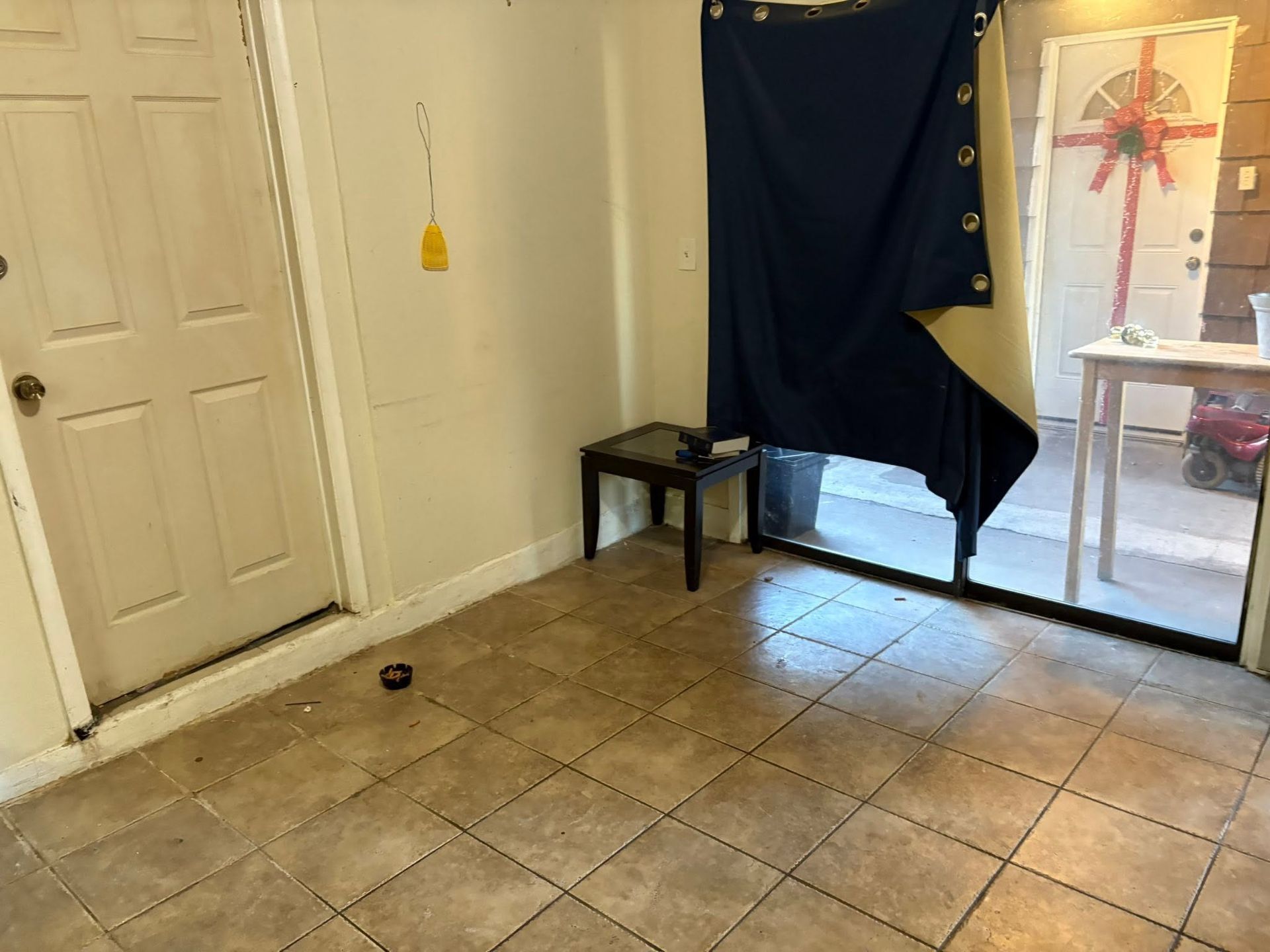 Small room with tiled floor, white door, dark curtain, and a table by a window.