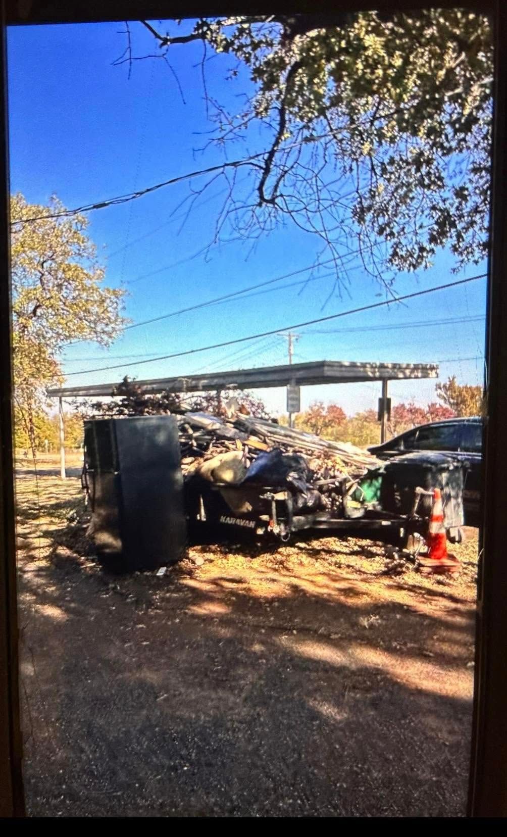 Burned-out vehicle remains in a wooded area near water under a clear blue sky