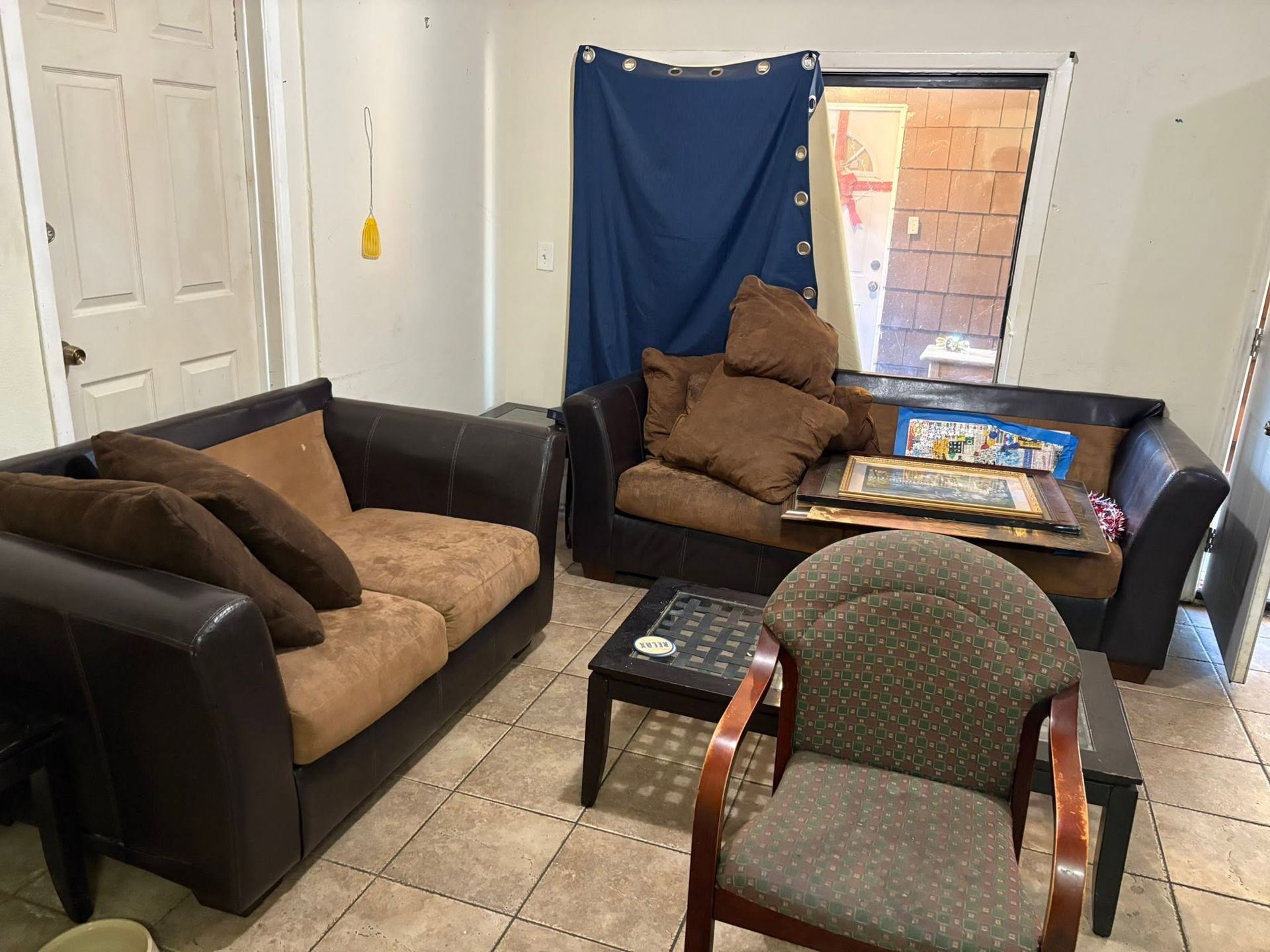 Living room with two sofas, a chair, and a table by a bright window with a blue curtain