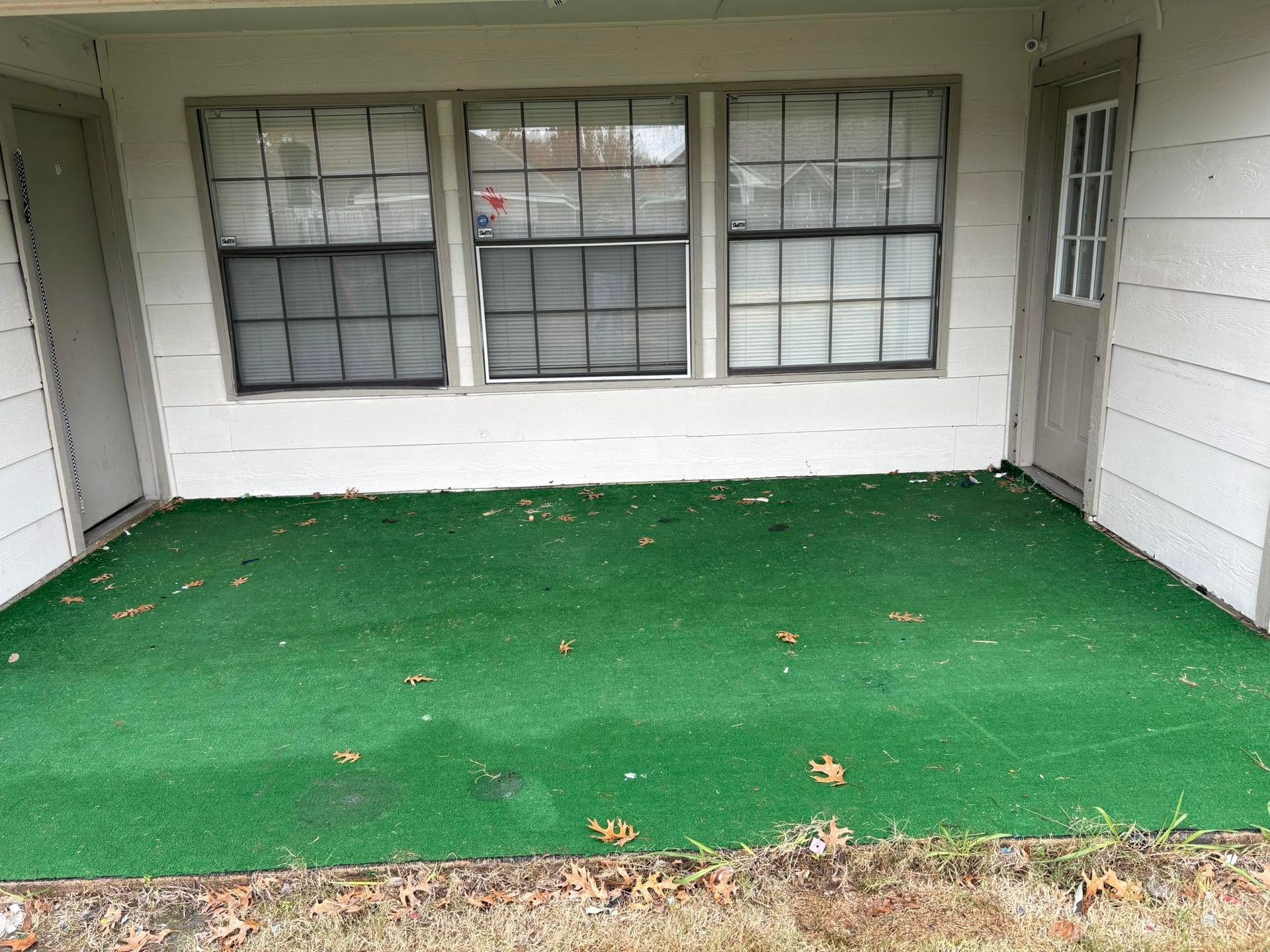 Covered porch with green artificial turf and white walls, viewed from the front.