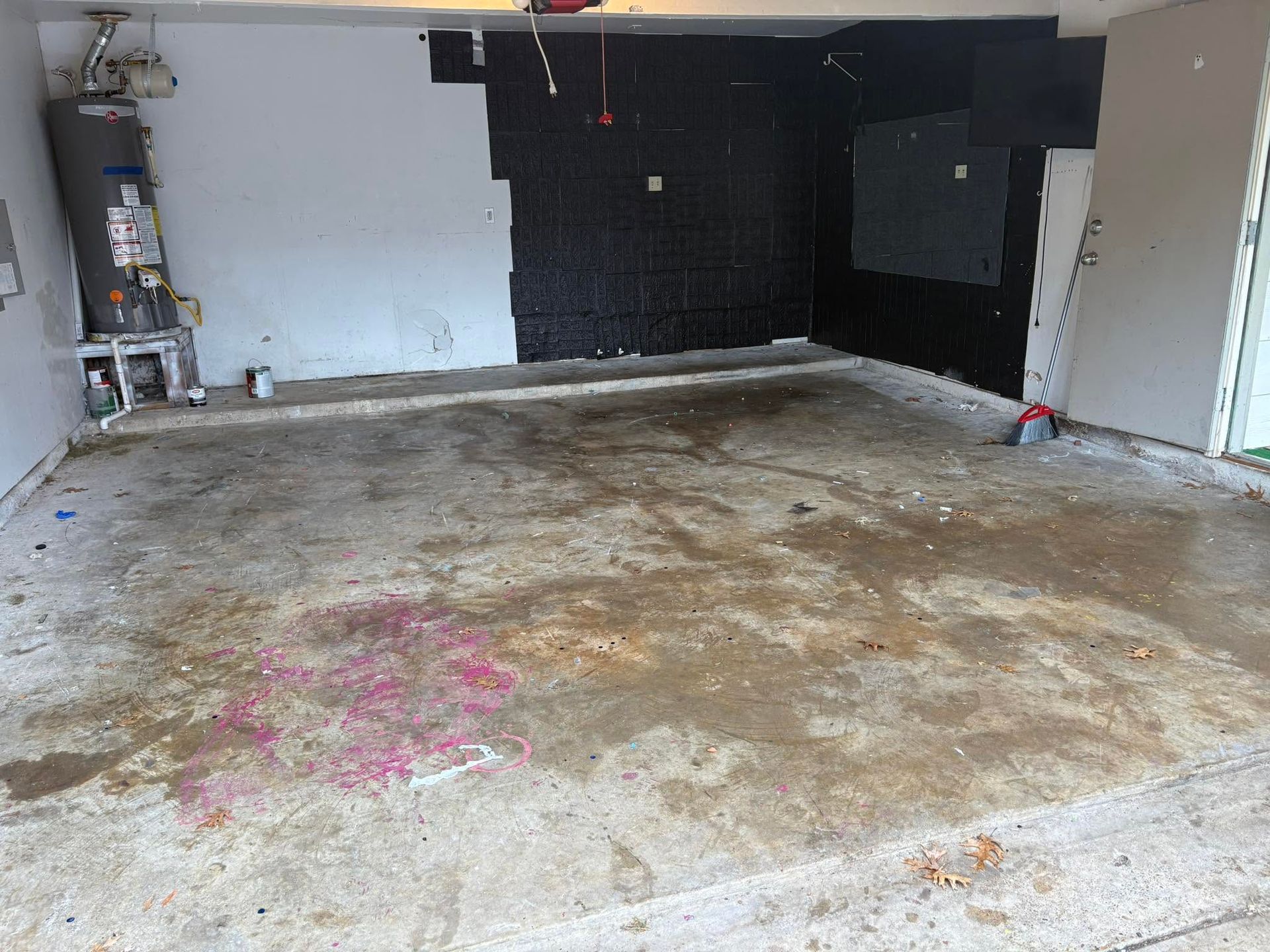 Empty garage with stained concrete floor and white walls, showing a cluttered utility area on the left.