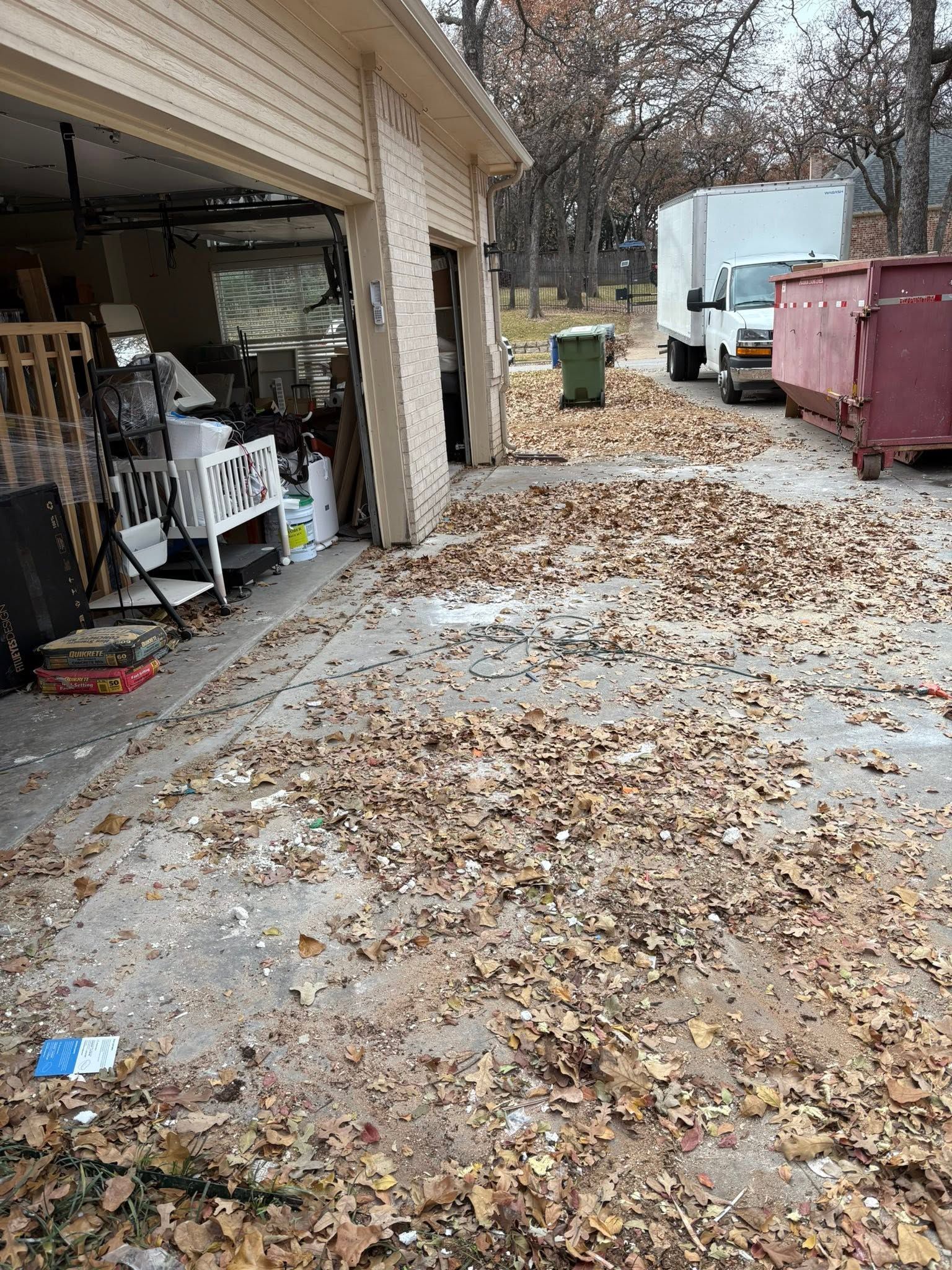 Leaf-covered driveway beside garage, with trash bins and a truck in the background.
