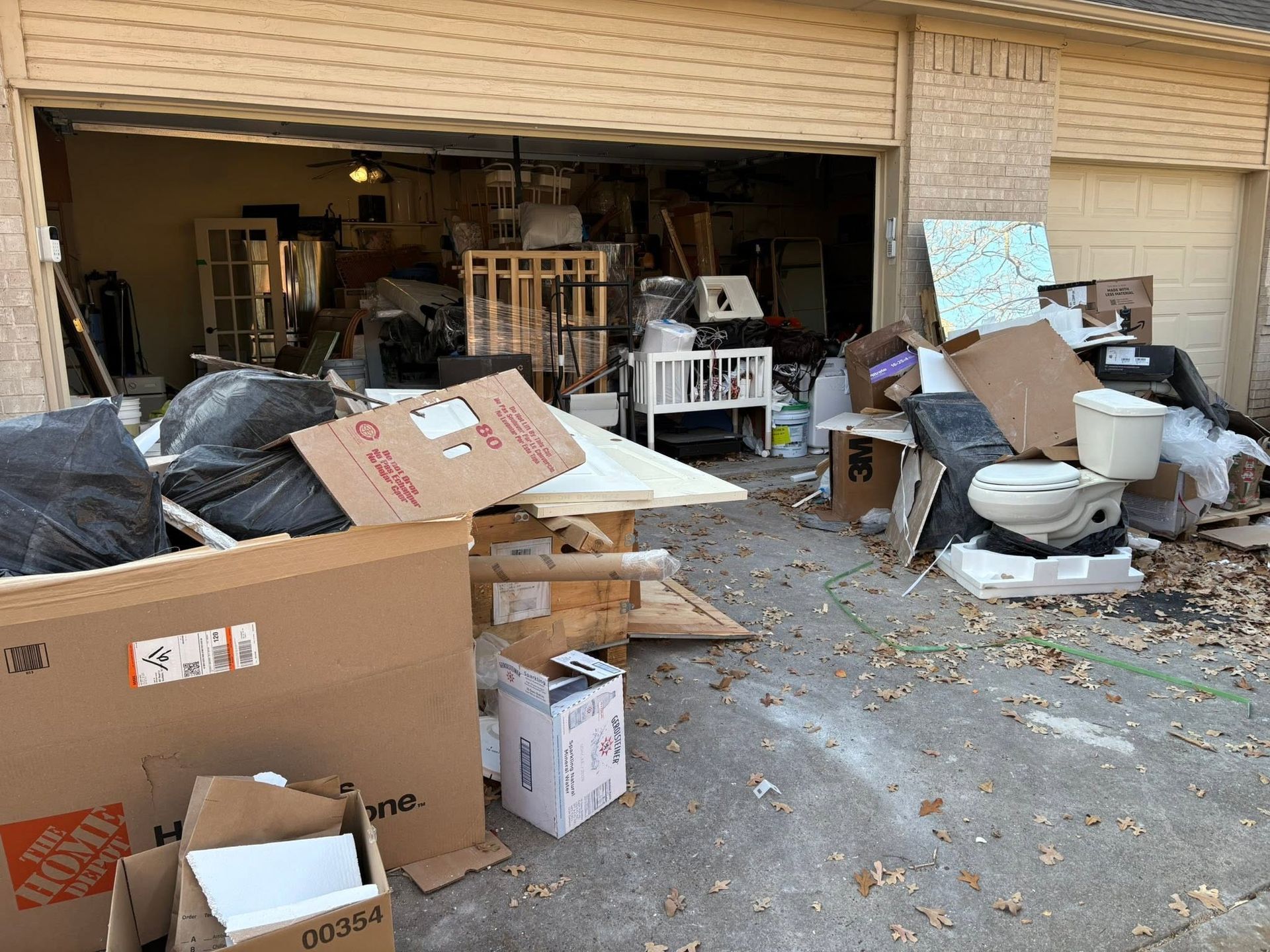 Garage overflowing with boxes, furniture, and trash, with debris spilling onto the driveway.