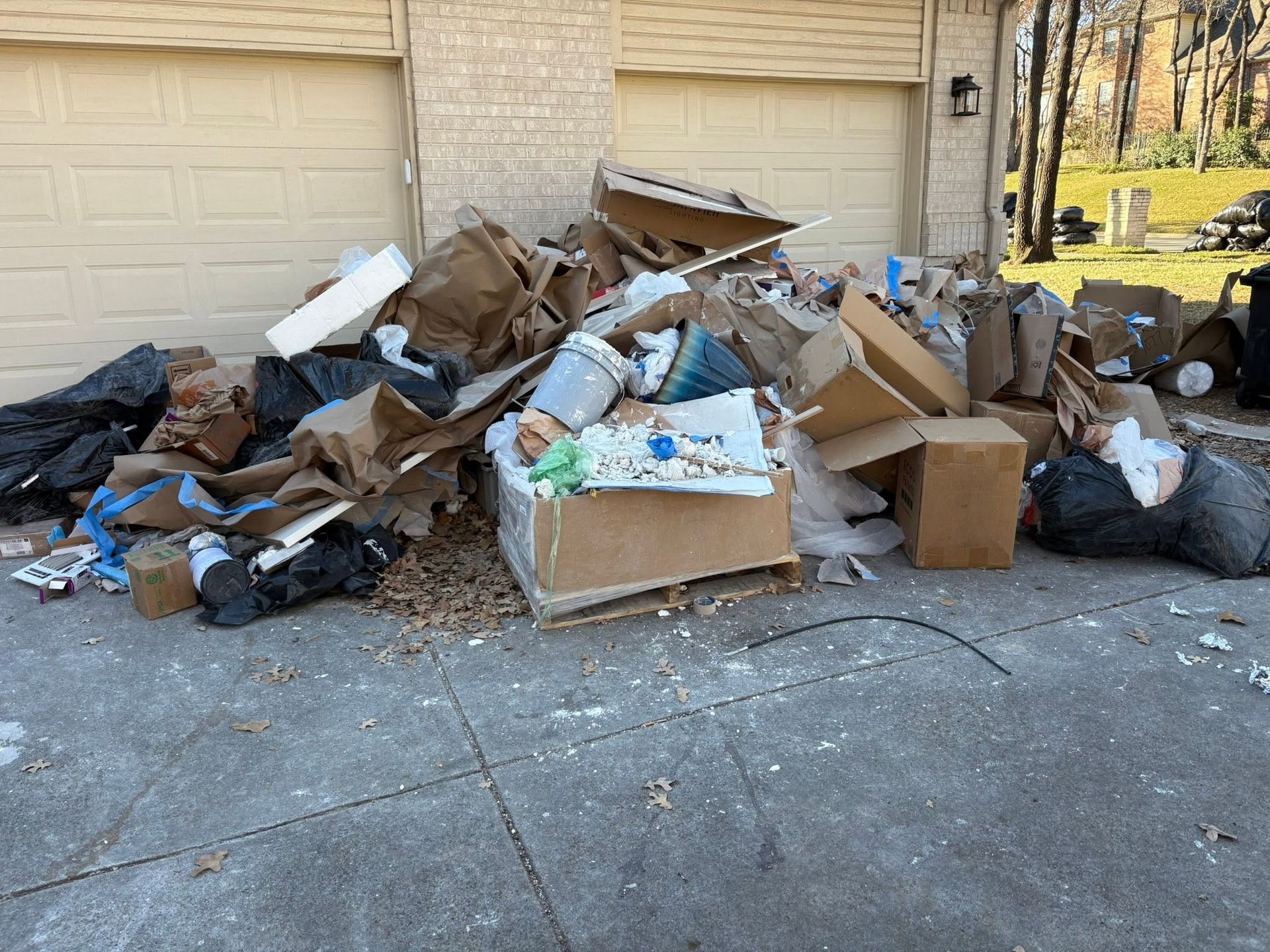 Overflowing trash and broken cardboard piled in a driveway before garage doors