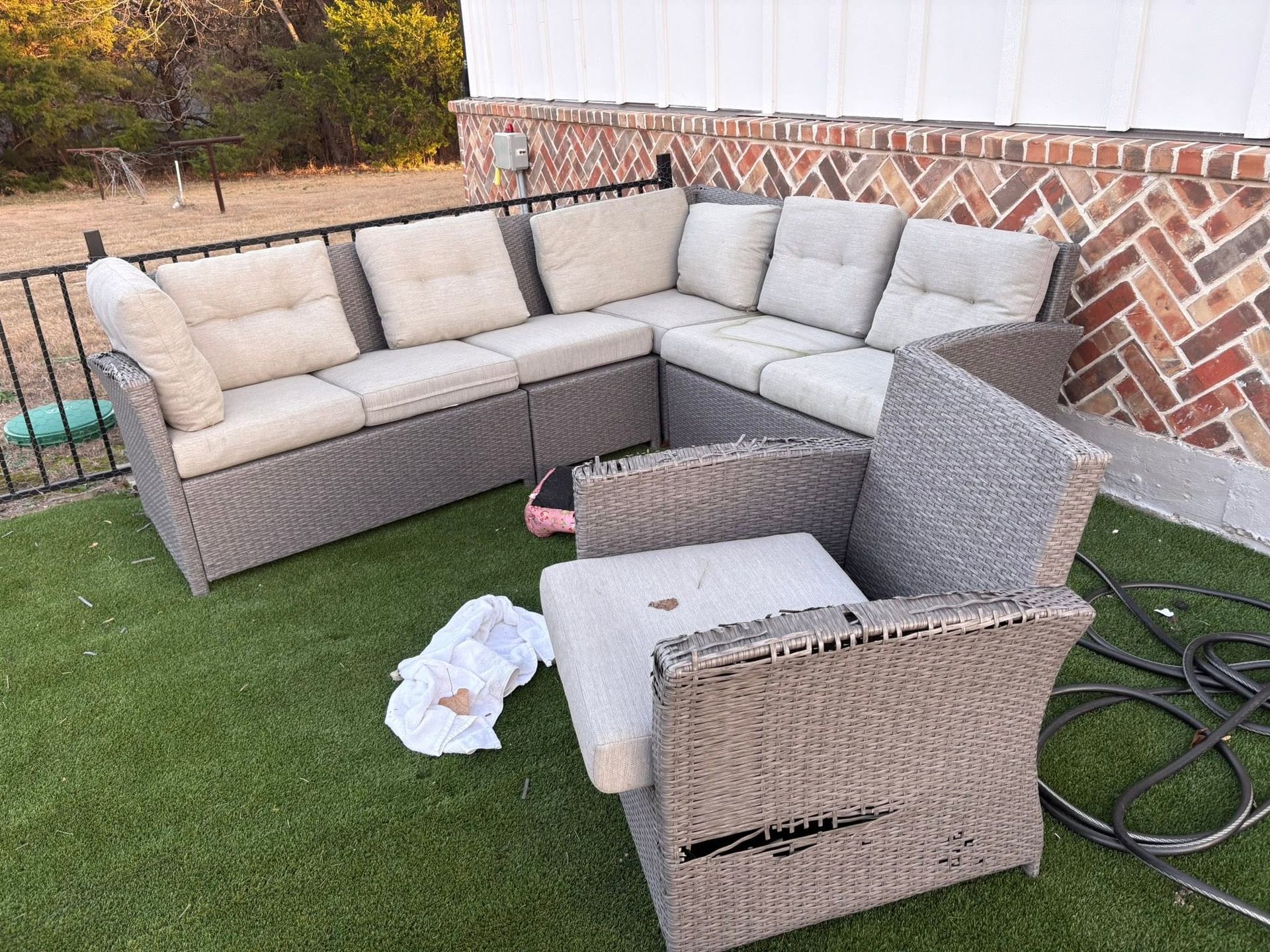 Outdoor wicker sectional sofa set on artificial grass, with cushions and a loose chair cushion by a brick wall.