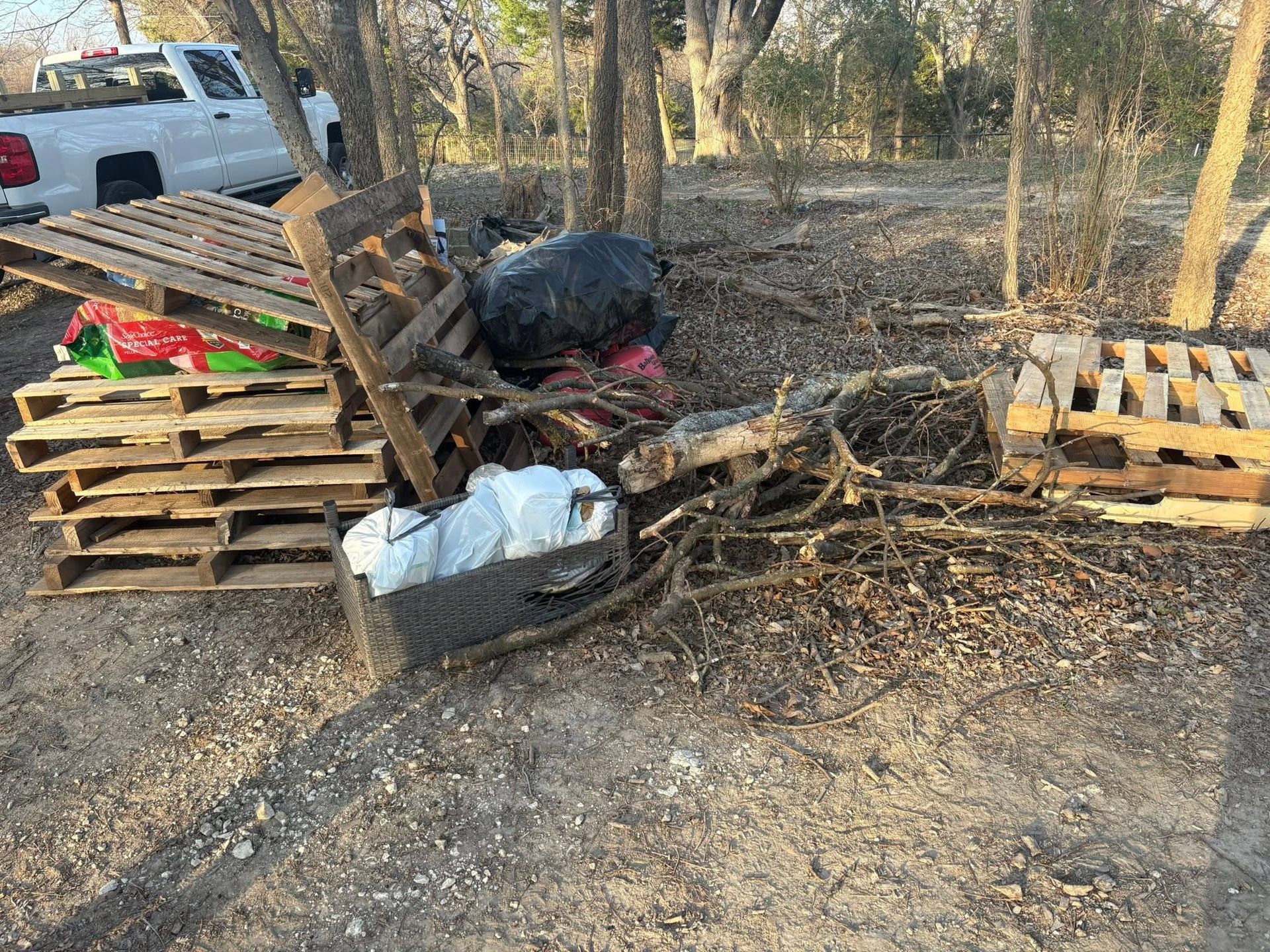 Scattered wooden pallets and debris beside a small brush fire in a wooded yard