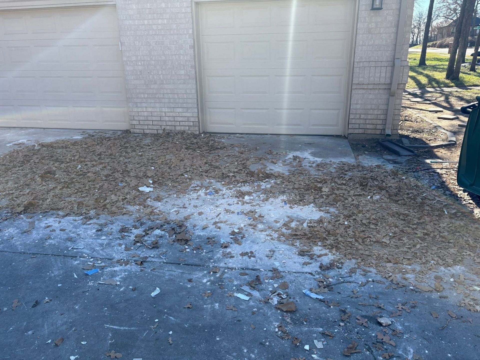 Snow-dusted driveway in front of a garage, with scattered ice and gravel on the ground.