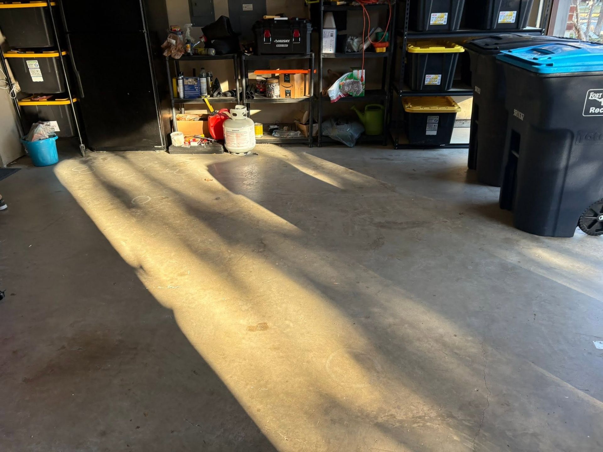 Sunlit garage floor with shelves, storage bins, and tools along the back wall