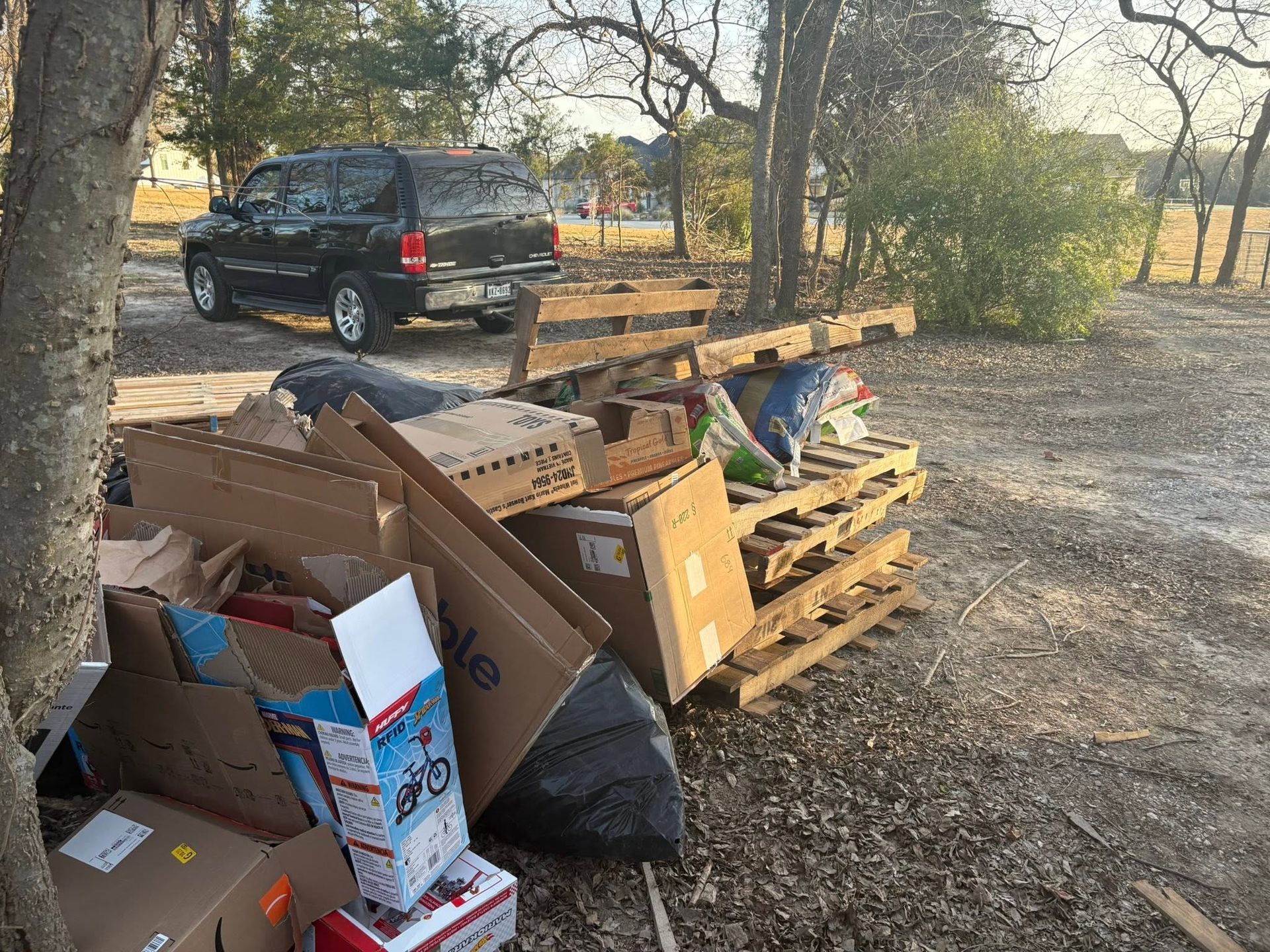 Discarded cardboard and trash piled beside a black van in a wooded outdoor area