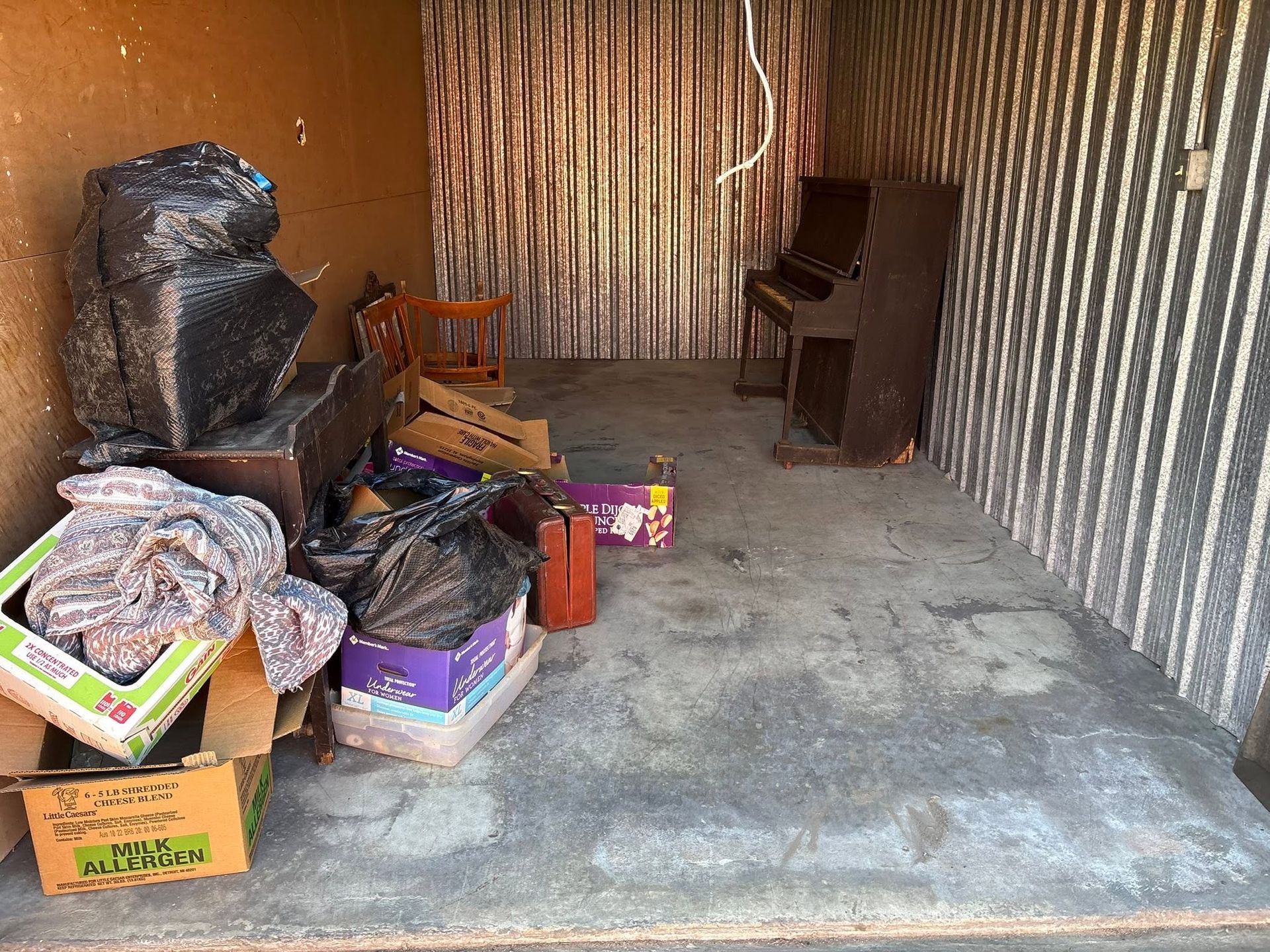 Storage unit with scattered boxes, bags, and furniture on a concrete floor.