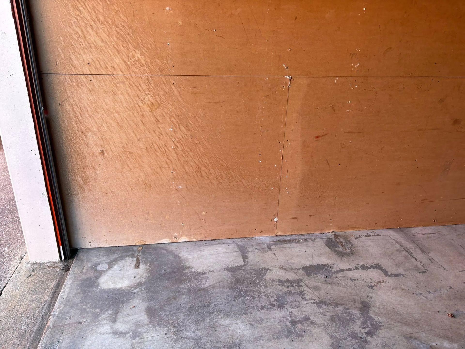 Close-up of a worn brown door with a concrete floor and a metal frame on the left.