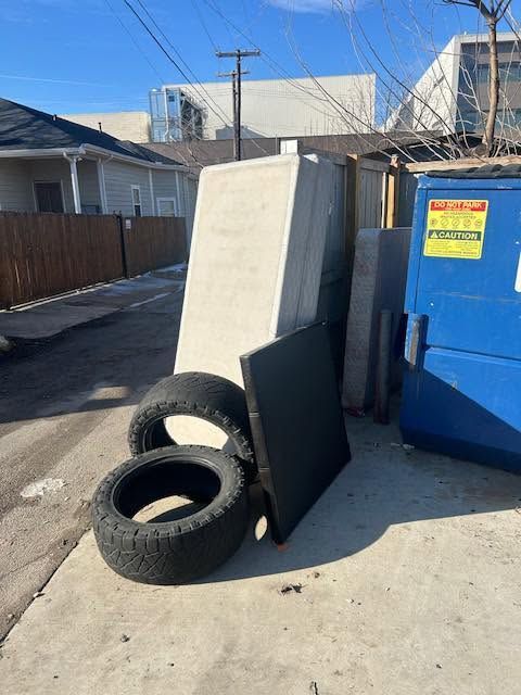 Two tires leaning against a large white board beside a blue dumpster in an alley