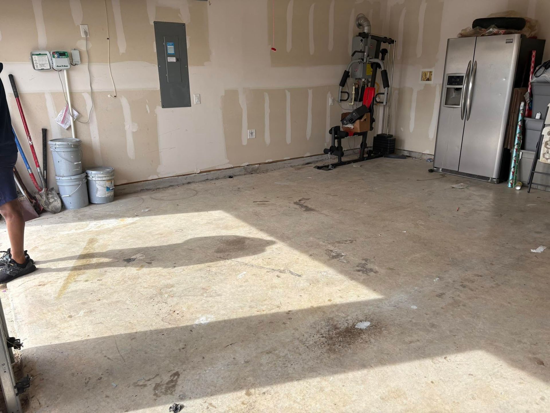 Empty garage with unfinished drywall, concrete floor, and tools stacked along the wall.