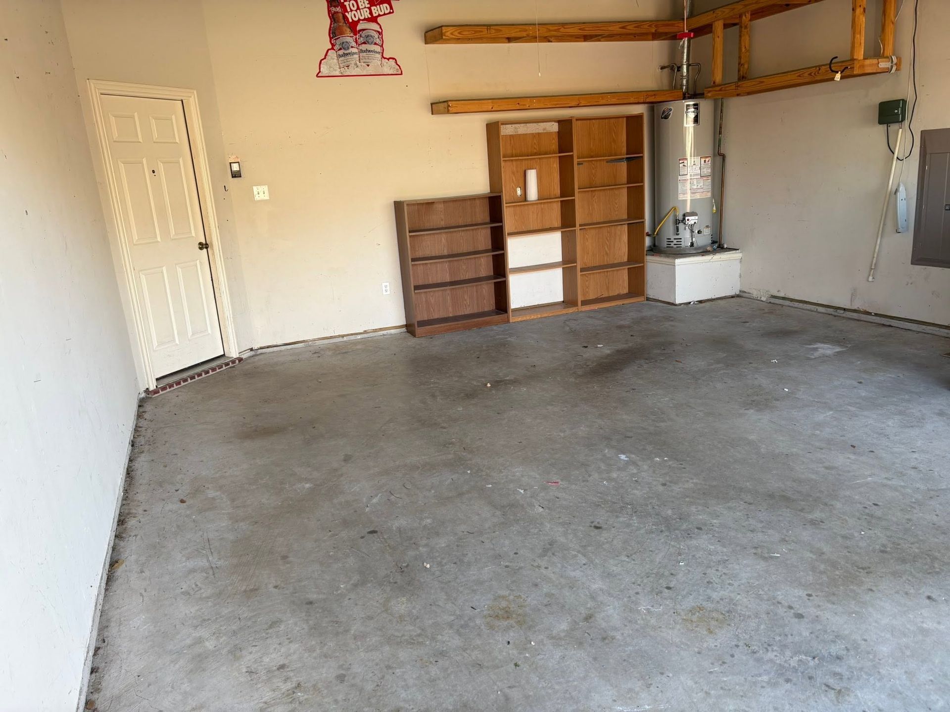 Empty garage with concrete floor, wood cabinets, shelving, and a water heater on the back wall