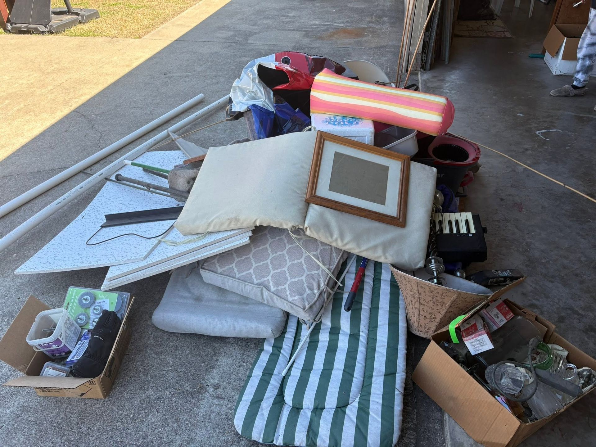 Scattered household items and cushions in cardboard boxes on a sidewalk near a curb
