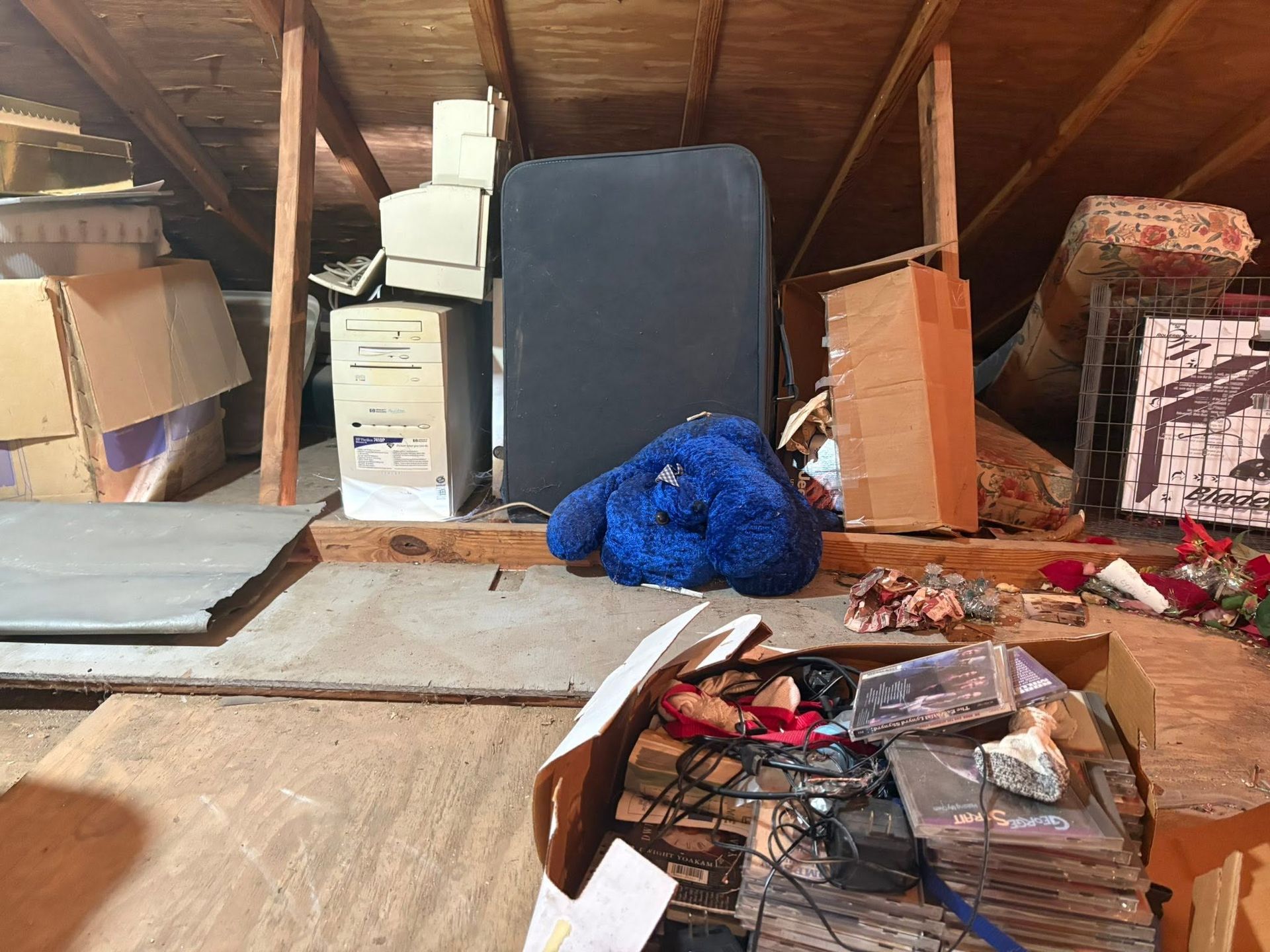 Cluttered attic with boxes, folded mattress, blue plush toy, and scattered items on the floor