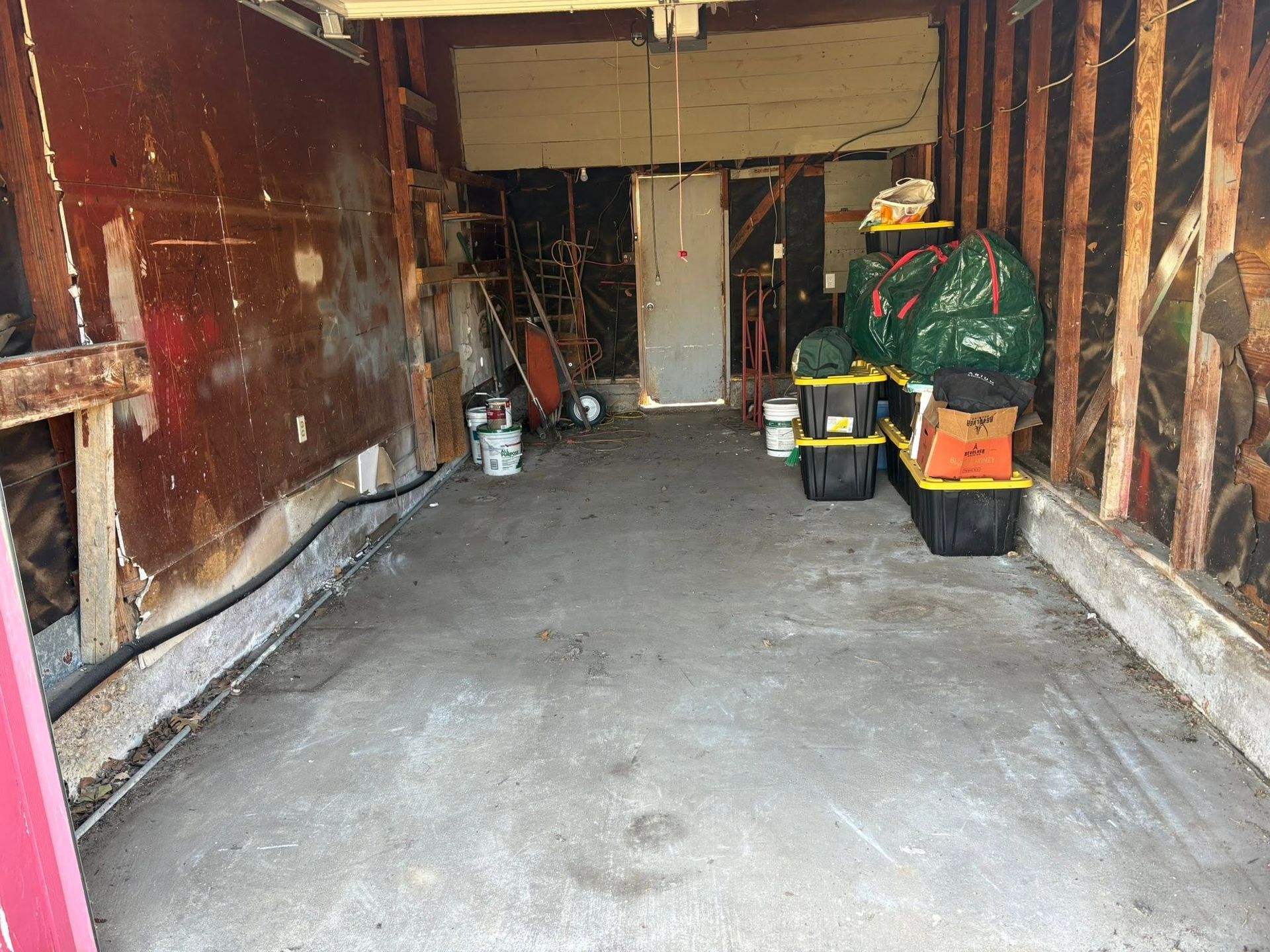 Empty unfinished garage with exposed studs, concrete floor, and storage bins along the walls