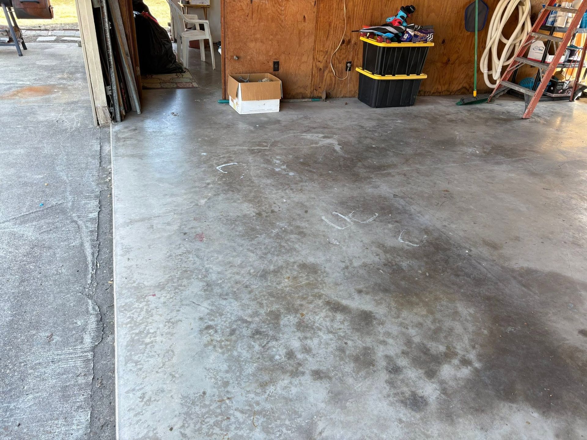 Concrete garage floor with dark stains, wooden wall, and storage bins along the back wall