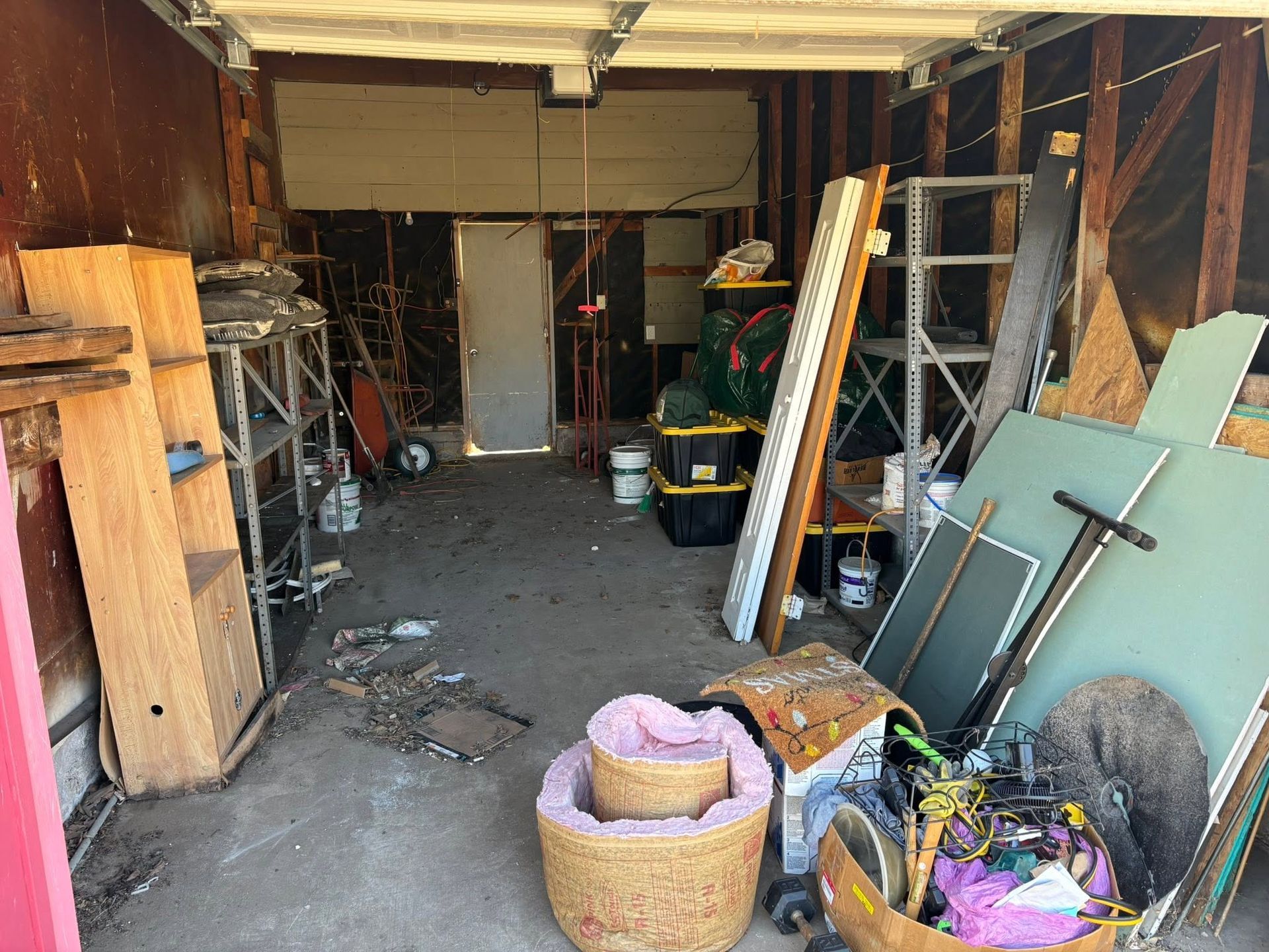 Cluttered garage with shelves, ladders, boxes, and tools along a narrow central aisle.