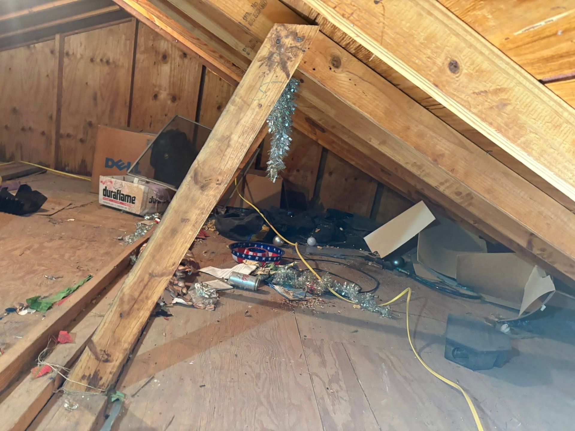Attic with exposed beams, clutter, and a large wooden support brace under the roof.
